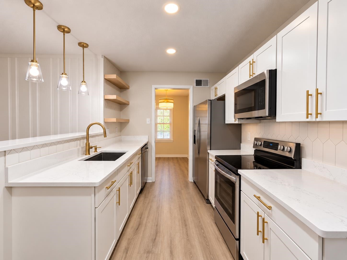 Renovated kitchen with white cabinets, brass fixtures, quartz counters, and stainless steel appliances.