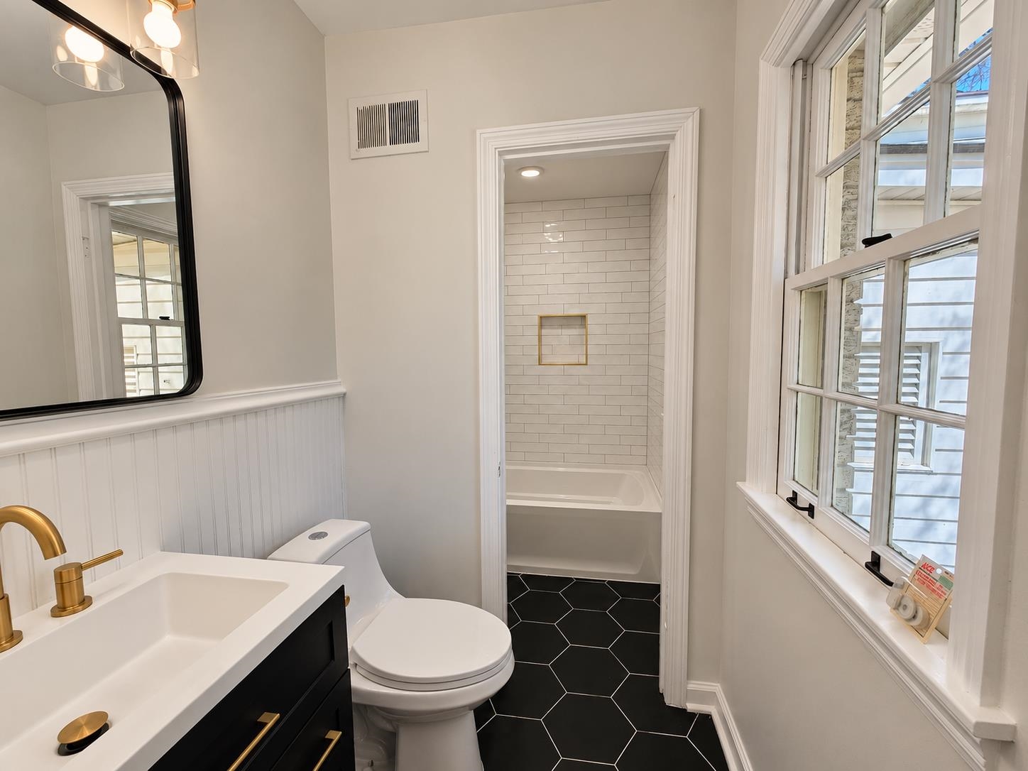 Bathroom with a black hexagonal tile floor, white subway-tile tub surround, and tall windows.