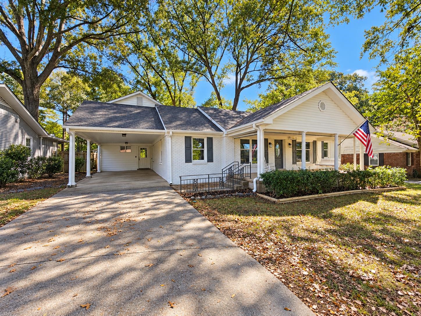 White brick single-story home with a covered porch, carport, and American flag.