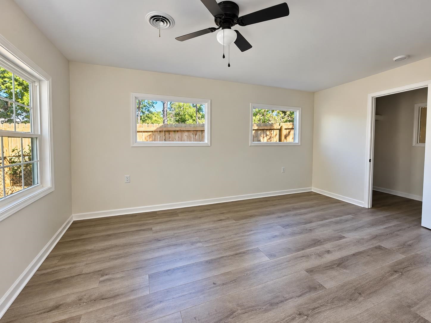 Empty room with plank flooring, multiple windows, and a black ceiling fan.
