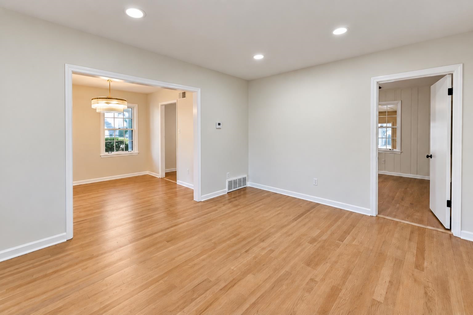 Empty room with hardwood floors and wide openings to adjoining rooms.