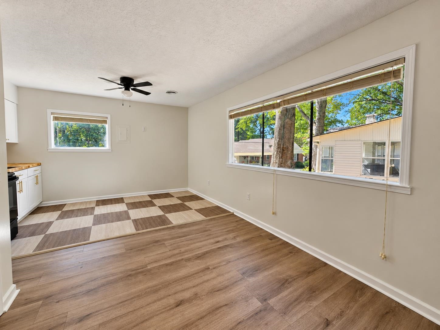 Vacant kitchen with checkered tile, wood-look floors, and large windows overlooking trees.