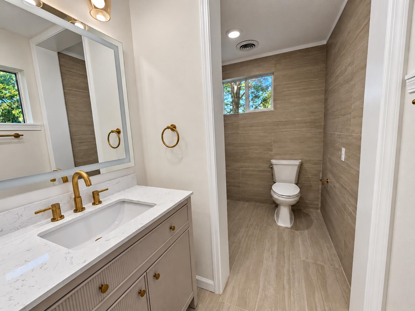 Bathroom with a white vanity, brass fixtures, and a taupe-tiled toilet alcove.