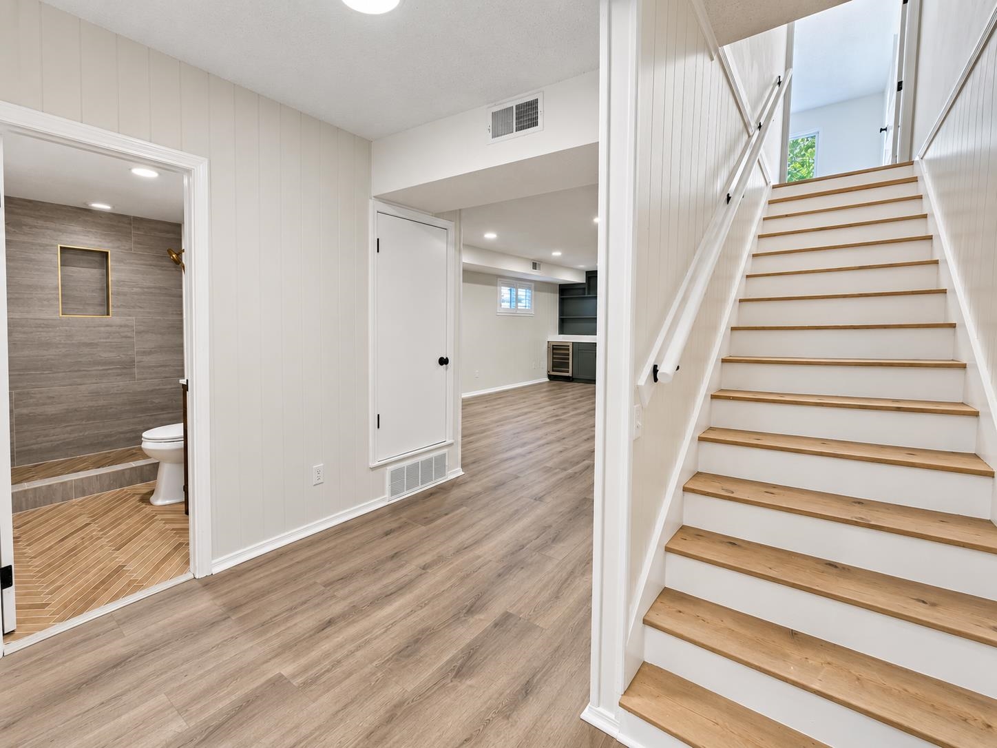 Finished lower level with a wood-tread staircase, tiled bathroom, and adjoining room with built-in shelves.