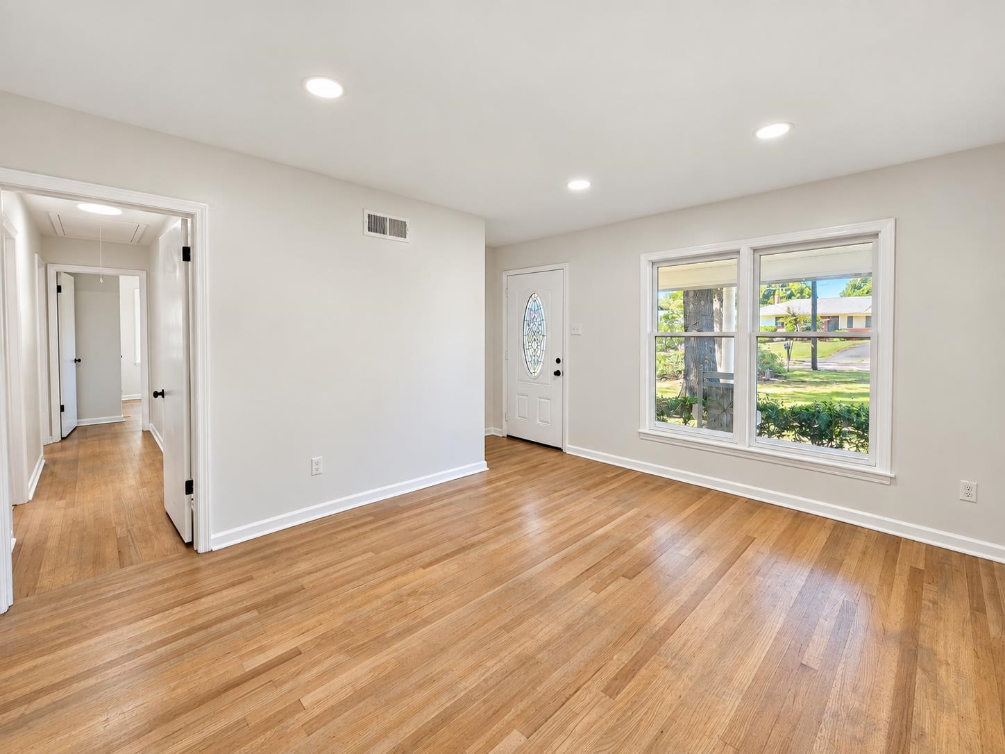 Empty room with hardwood floors, large windows, and a front door with an oval glass insert.