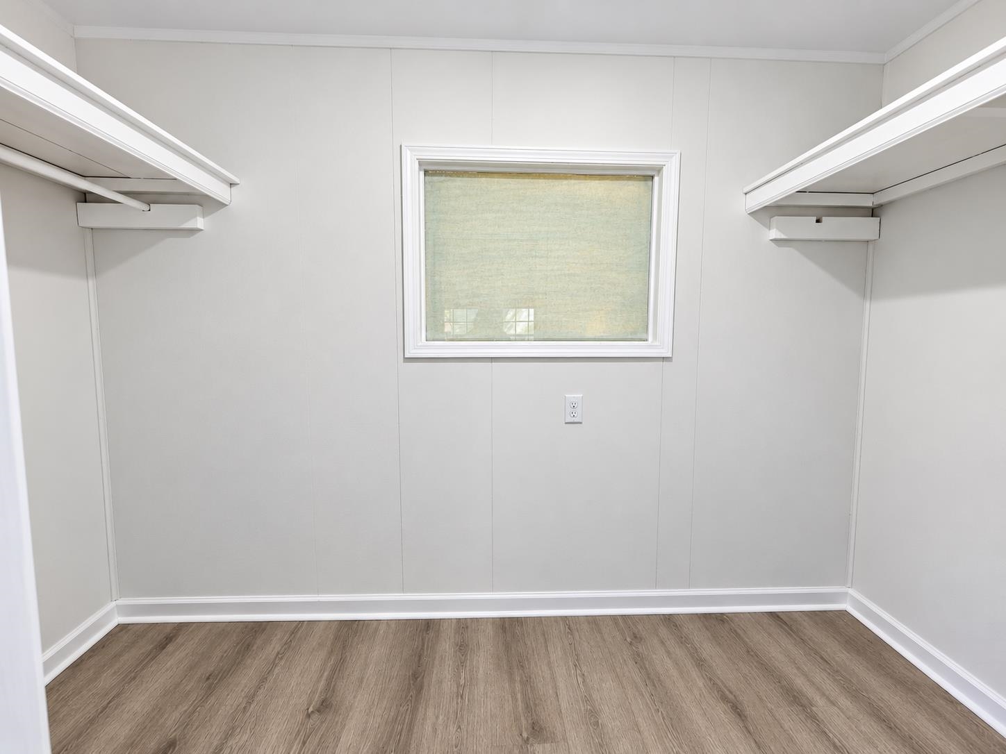 Walk-in closet with built-in shelves and hanging rods on both sides of a window.