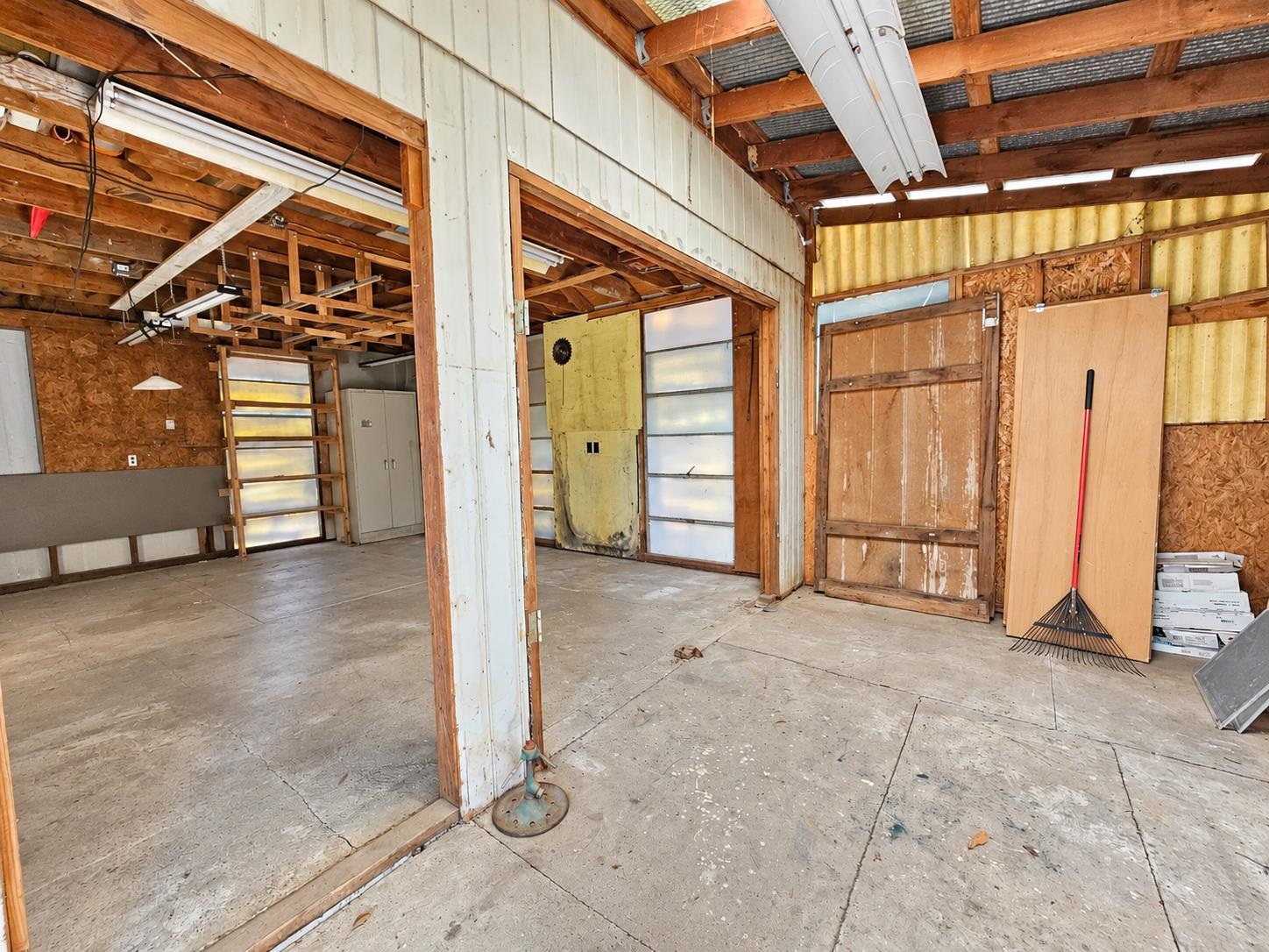 Unfinished garage interior with exposed timber framing, concrete floor, and fluorescent lights.