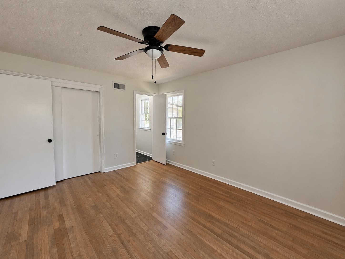 Empty bedroom with hardwood floors, a wood-blade ceiling fan, and a wide sliding-door closet.