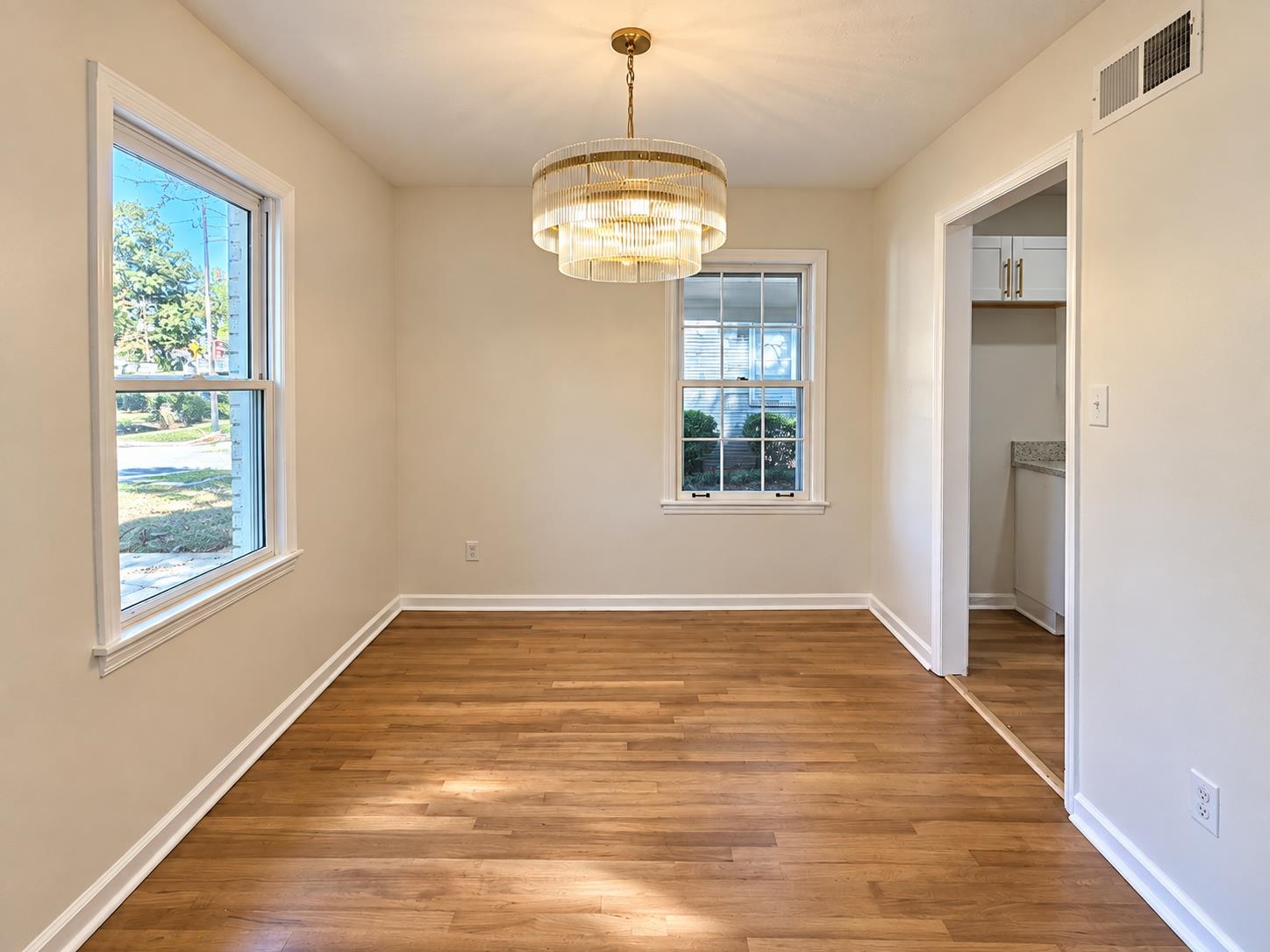 Empty dining room with wood floors, two windows, and a tiered chandelier.