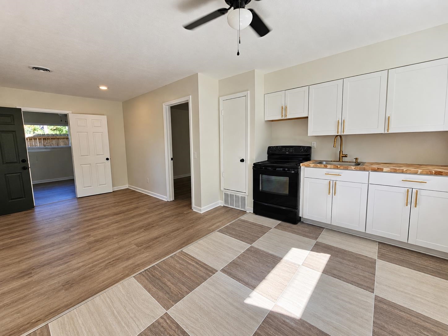 Vacant kitchen with white cabinets, a black range, butcher-block counters, and sunlight across the tiled floor.