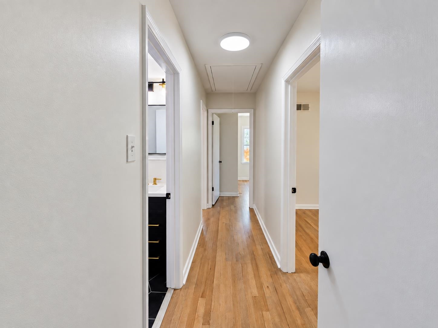 Interior hallway with warm hardwood floors, white walls, and open doorways to adjoining rooms.