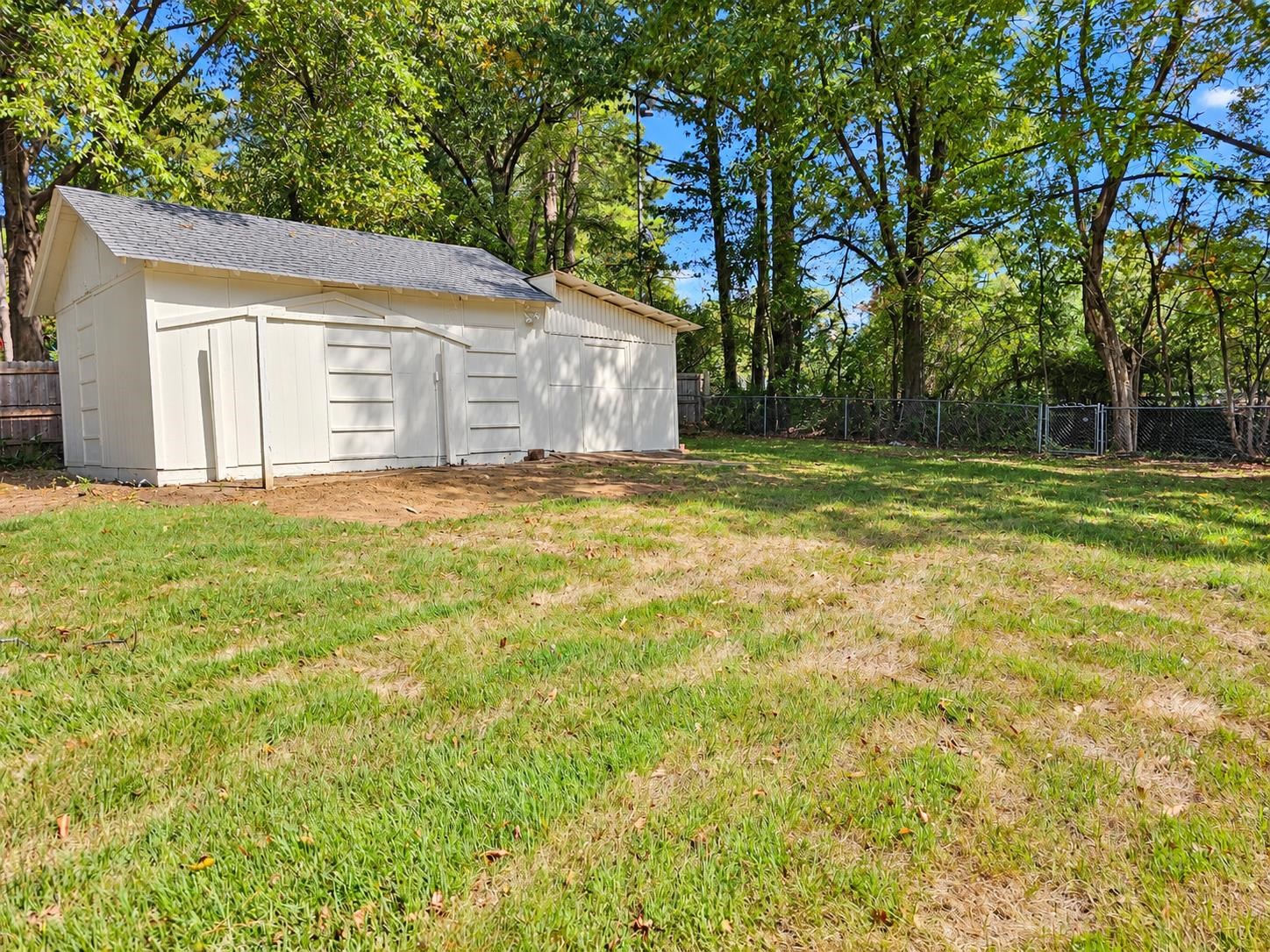 White backyard storage shed with multiple doors, surrounded by grass and mature trees.