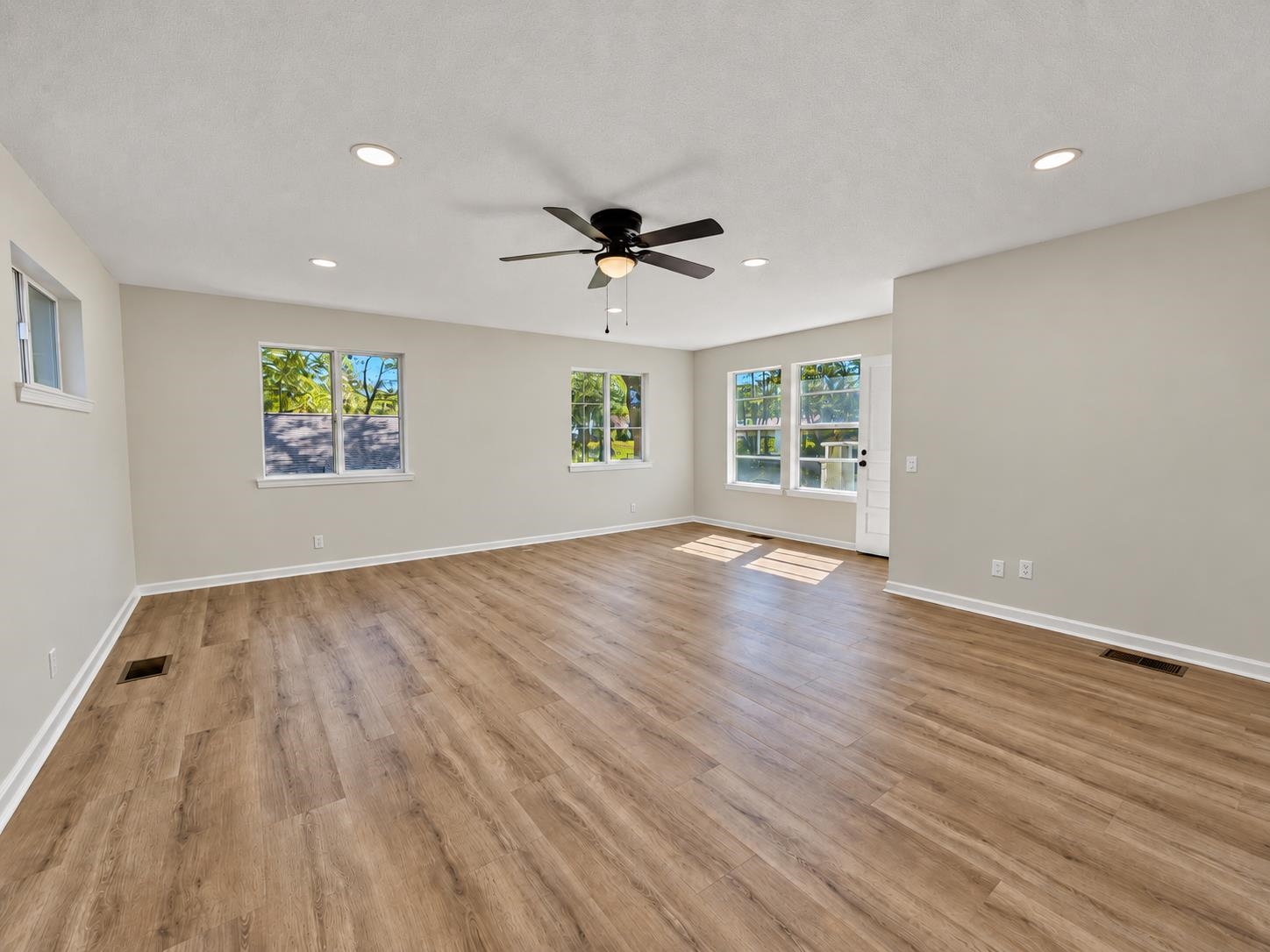 Vacant living room with wood-look floors, multiple windows, and a ceiling fan.