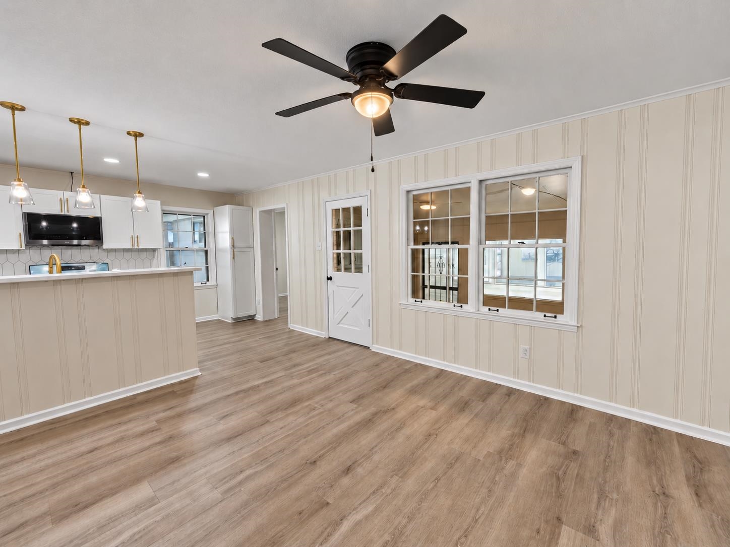 Unfurnished dining area beside a white kitchen, with wood-look flooring and a black ceiling fan.