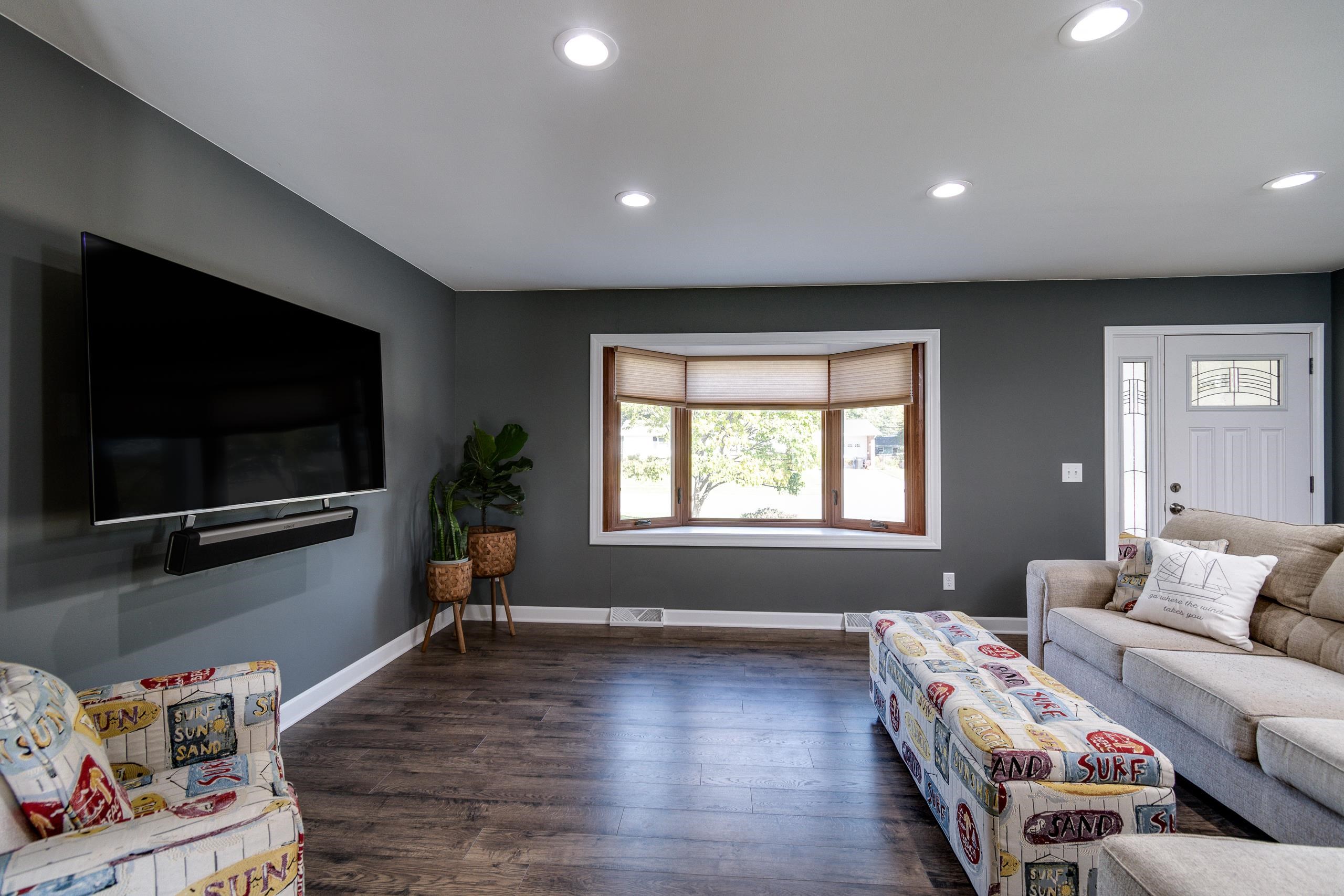 Living room with a bay window, dark gray walls, wall-mounted TV, and surf-themed seating.