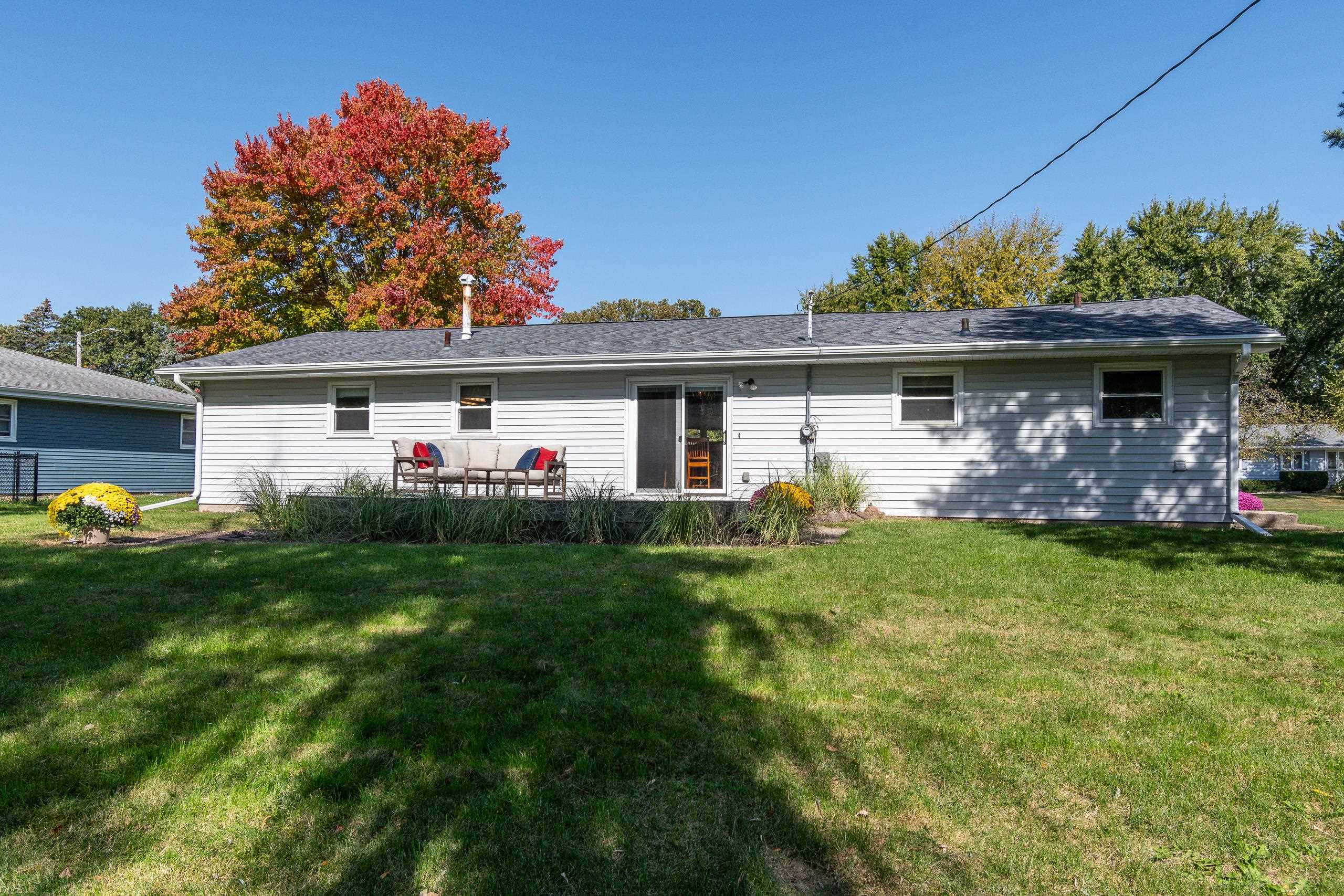 Rear of a single-story home with patio seating, landscaped garden beds, and an autumn tree.