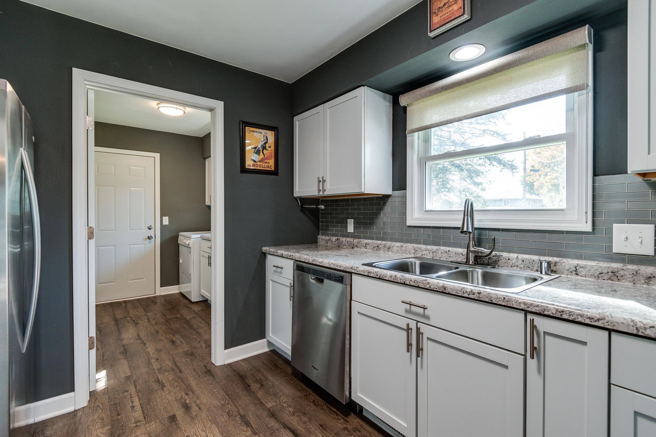 Kitchen with white cabinets, granite counters, and a double sink beneath a large window.