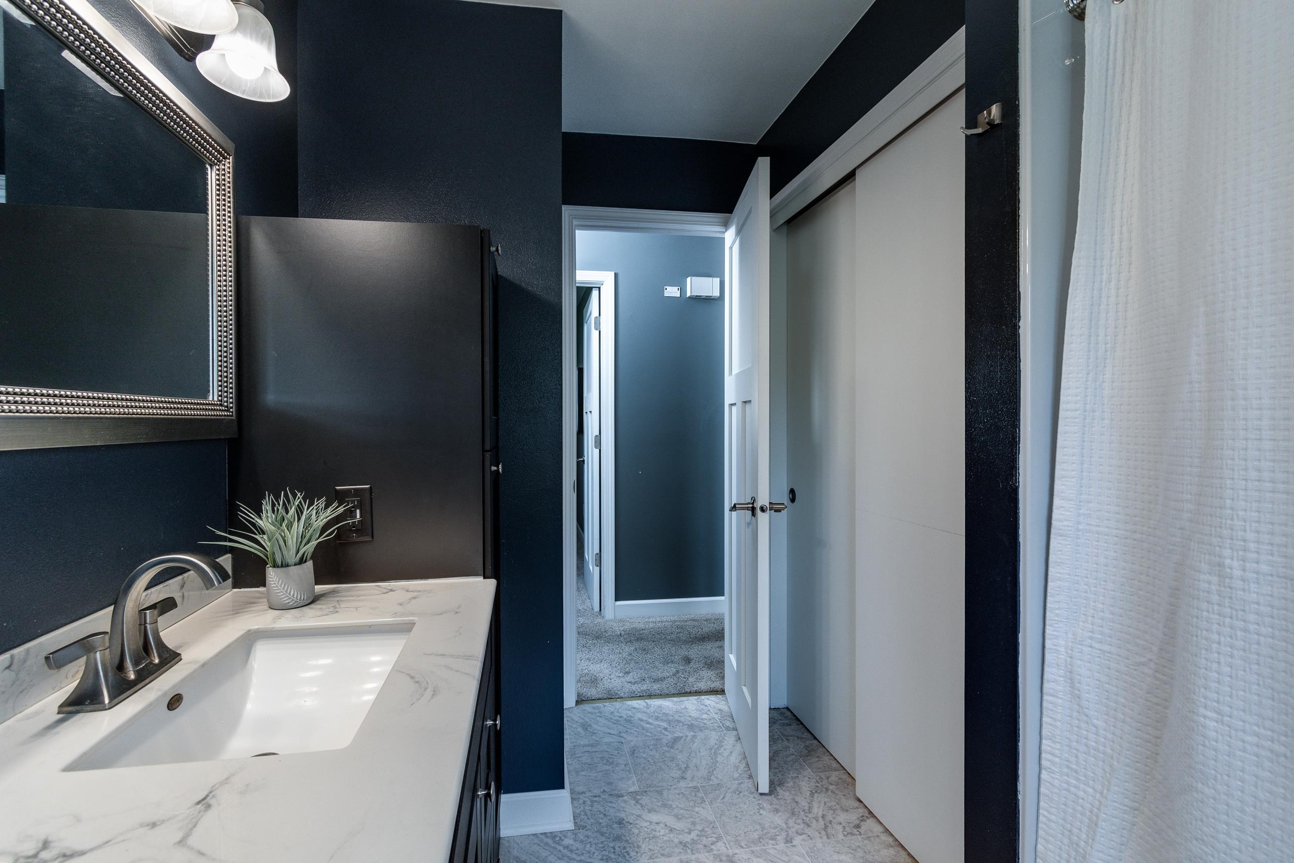 Bathroom with a marble-look vanity, dark navy walls, gray tile floor, and doorway to a carpeted room.