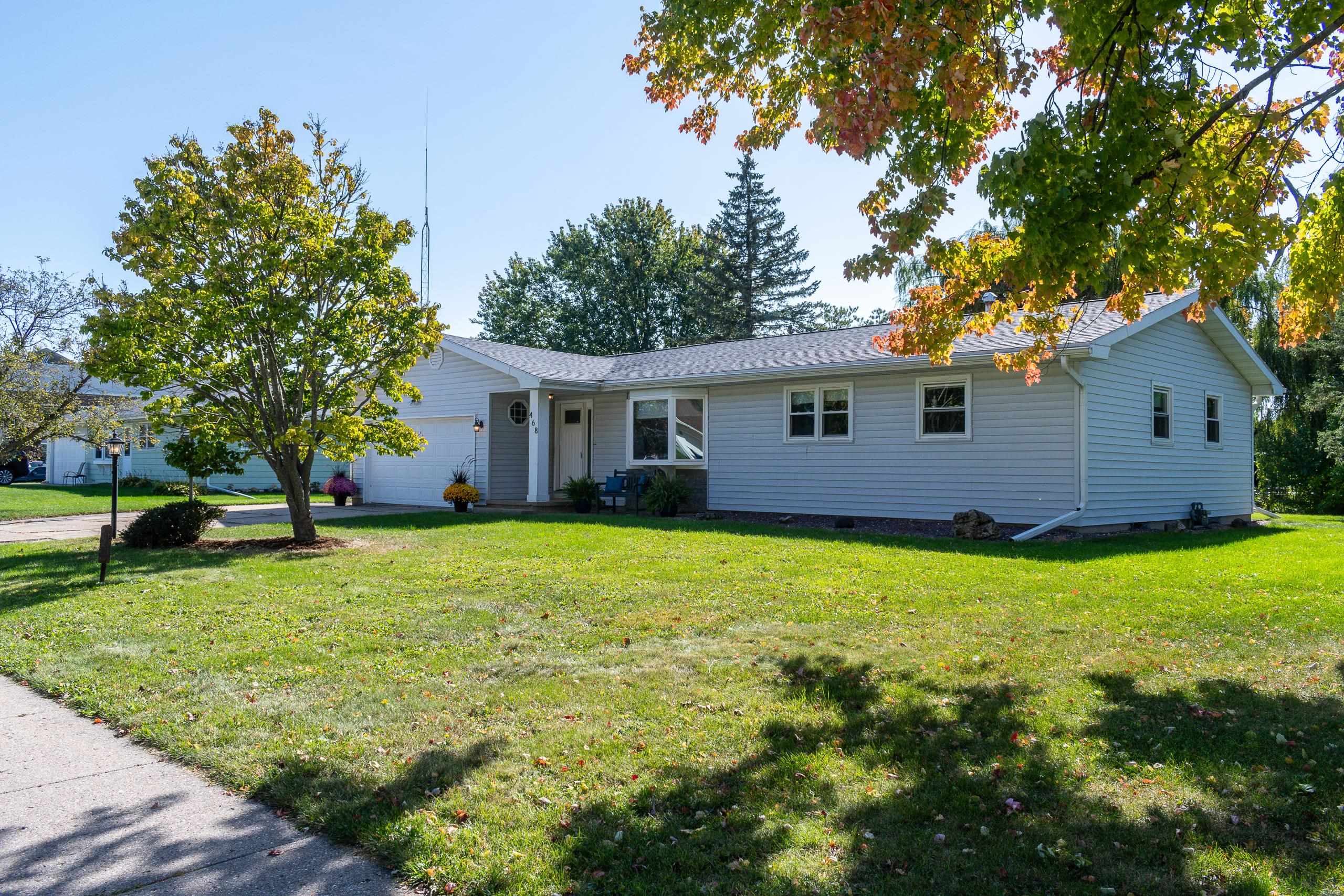 Single-story gray house with attached garage, broad front lawn, and autumn trees.