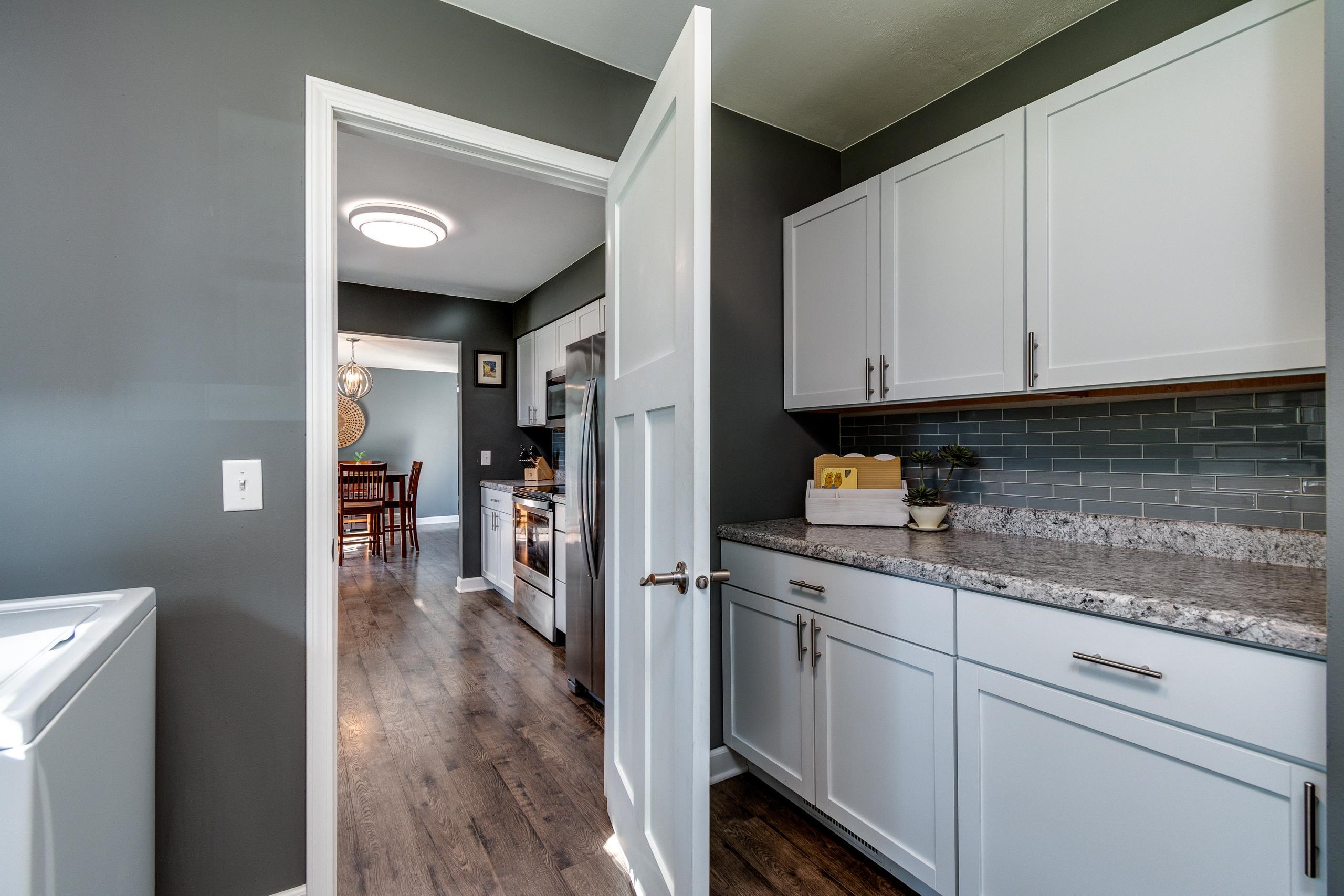 Kitchen with white cabinets, gray tile backsplash, granite counters, and a view through to the dining area.