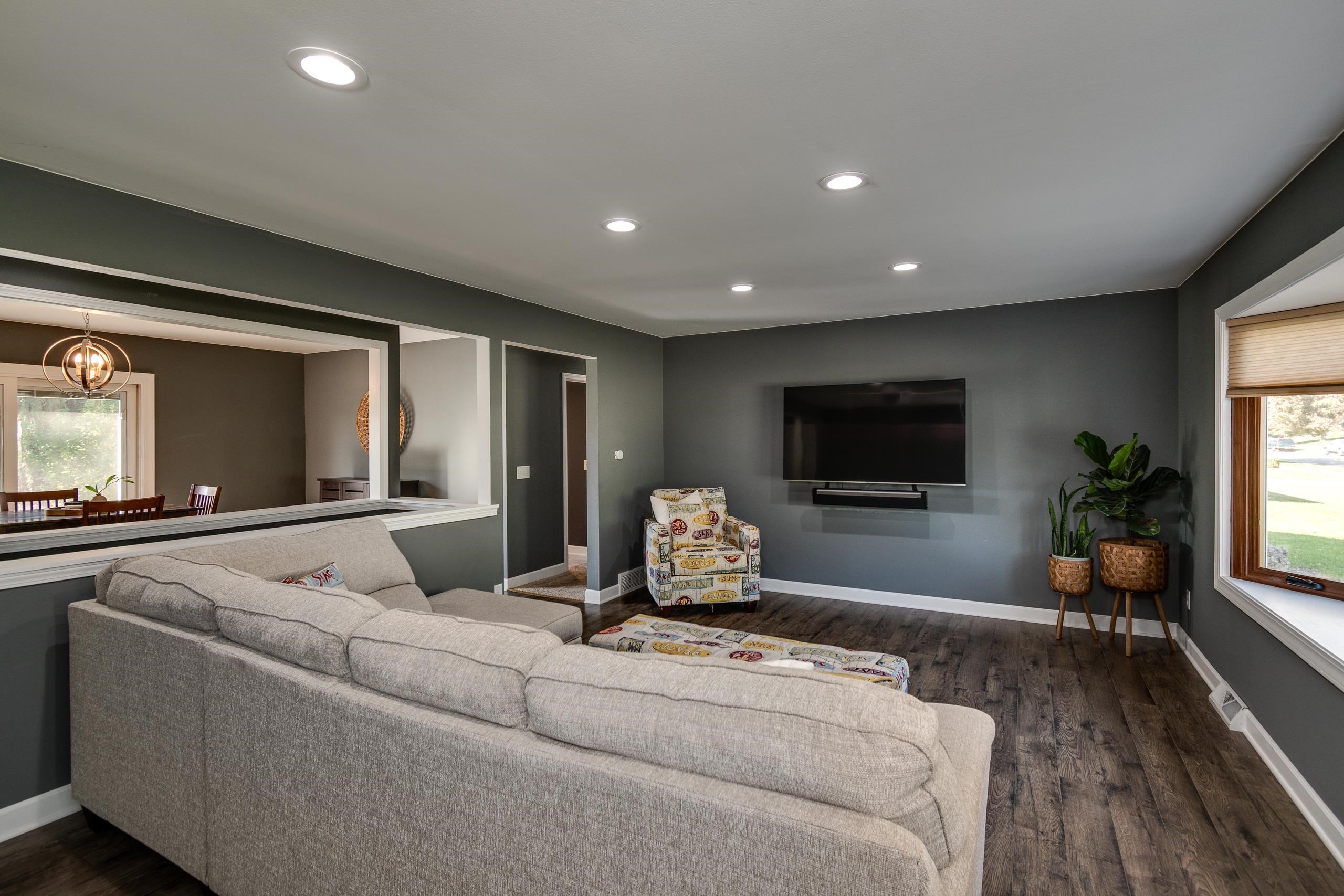 Living room with a large gray sectional, wall-mounted television, patterned chair, and plants.