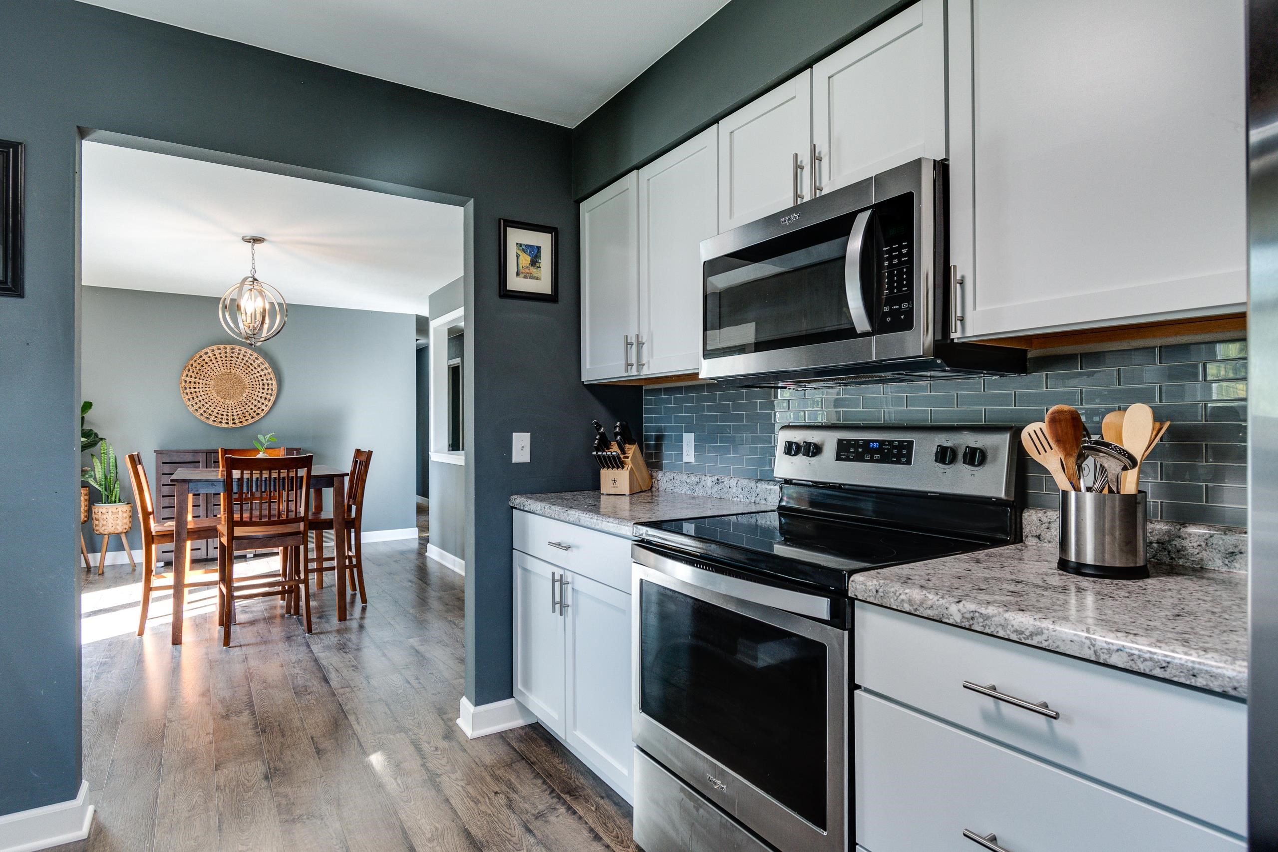 Kitchen with white cabinetry, stainless steel appliances, gray tile backsplash, and adjoining dining area.
