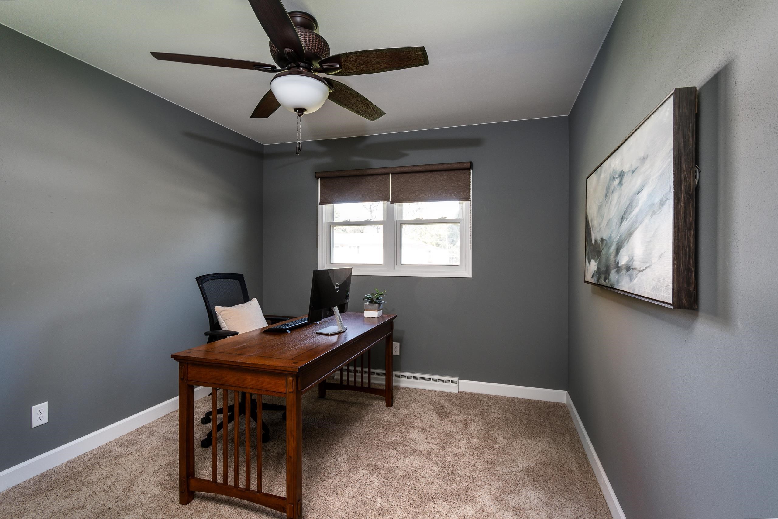 Home office with a wooden desk beneath a window and a ceiling fan overhead.