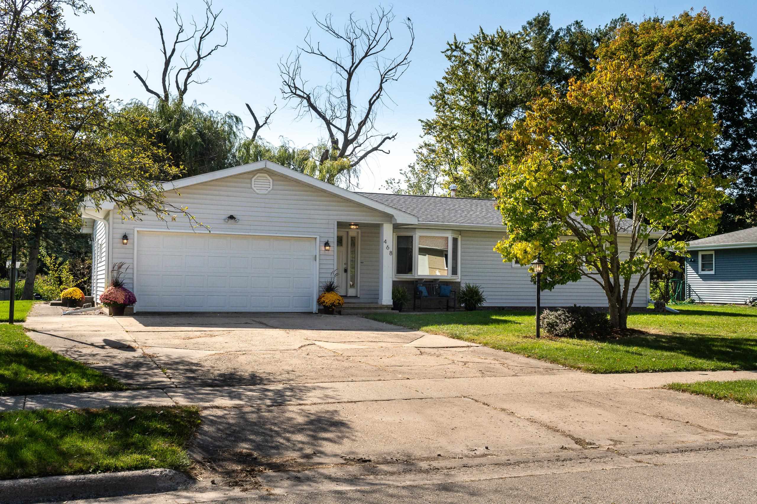 White single-story home with a two-car garage, broad driveway, and autumn trees.