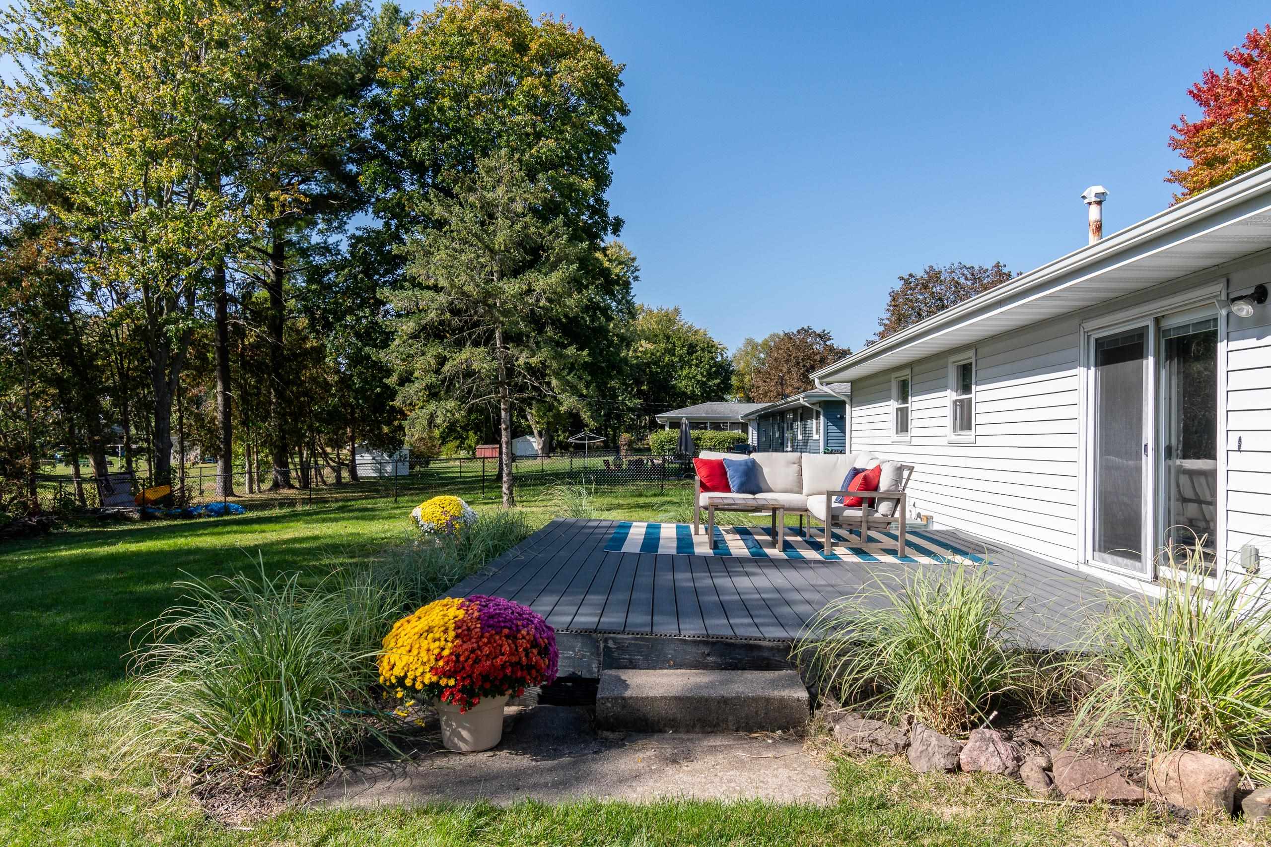 Backyard deck with outdoor seating, colorful chrysanthemums and a tree-lined lawn.