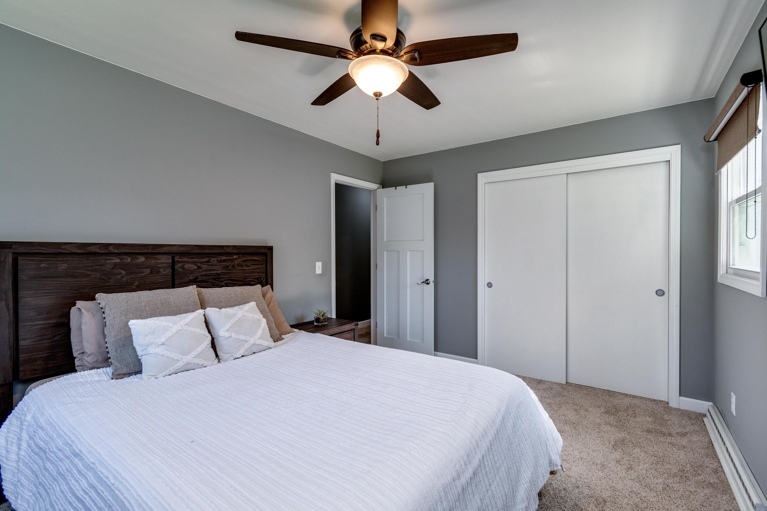 Bedroom with white bedding, a dark wood headboard, gray walls, and a ceiling fan.