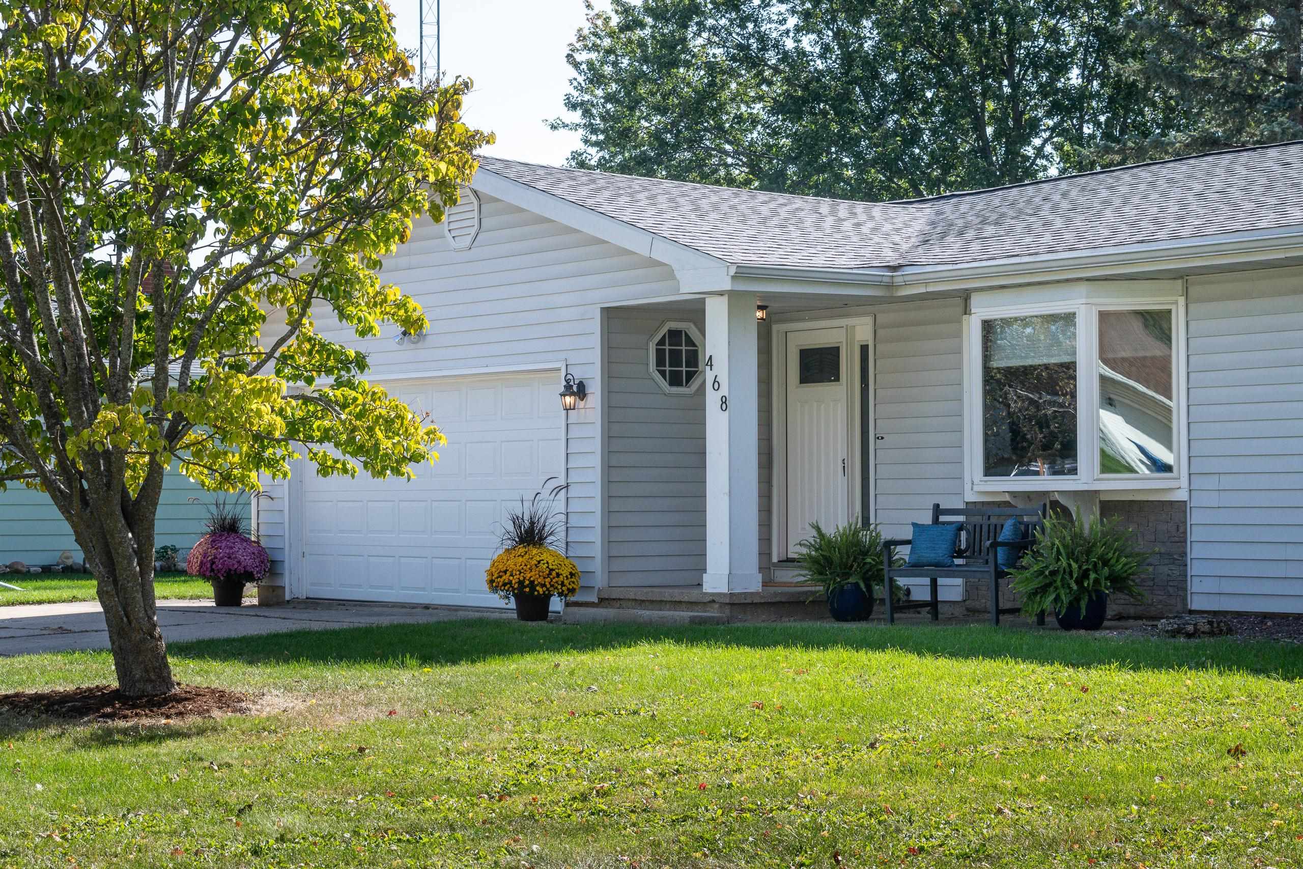 Light-gray single-story home with a two-car garage, covered entry, and landscaped front lawn.