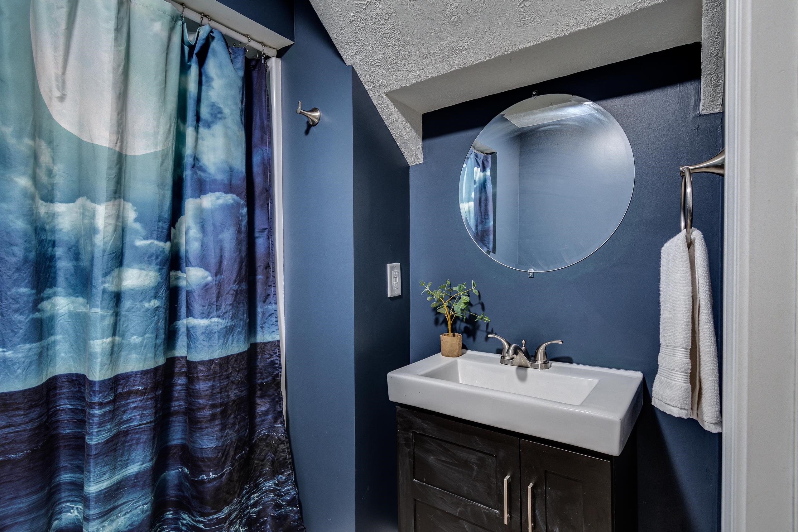 Bathroom with a white sink, round mirror, and blue cloud-patterned shower curtain.