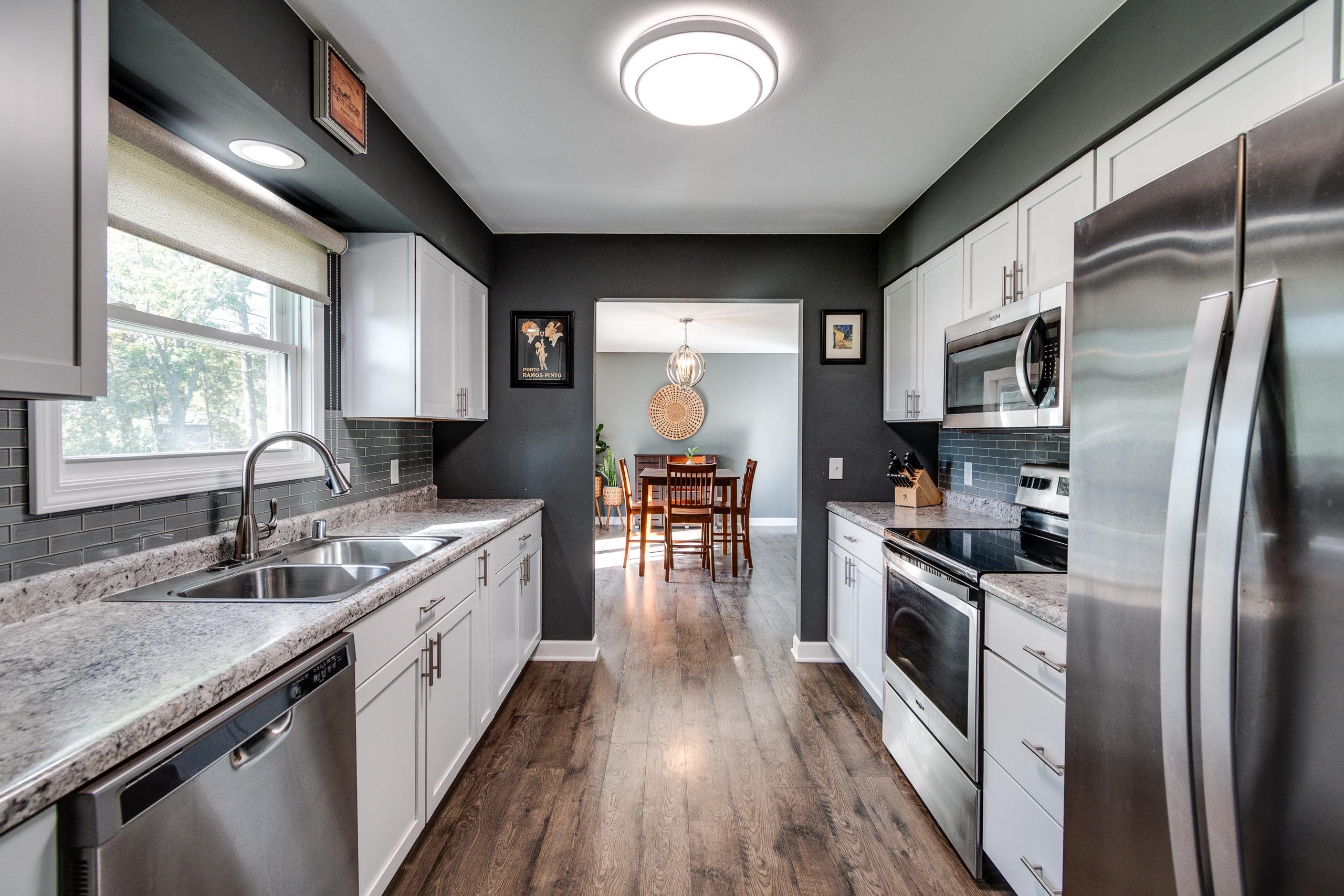 Modern kitchen with white cabinets, granite counters, stainless steel appliances, and a dining area beyond.