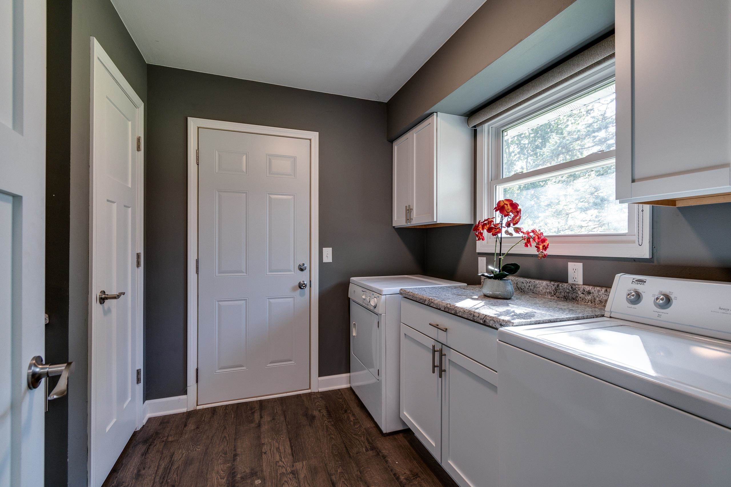 Laundry room with white washer and dryer, gray cabinets, and a countertop beneath a large window.