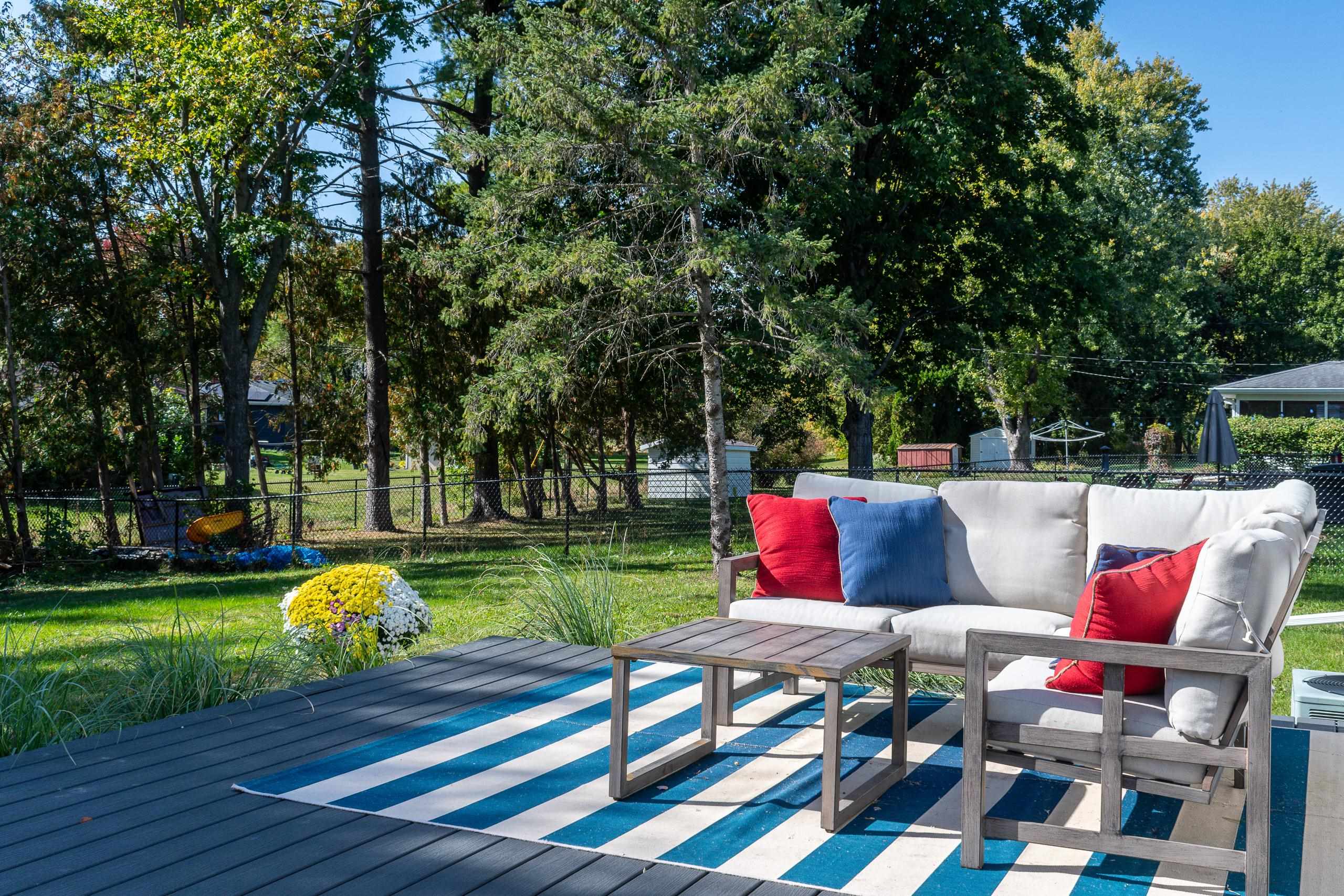 Backyard deck seating with red and blue cushions overlooks a leafy fenced yard.