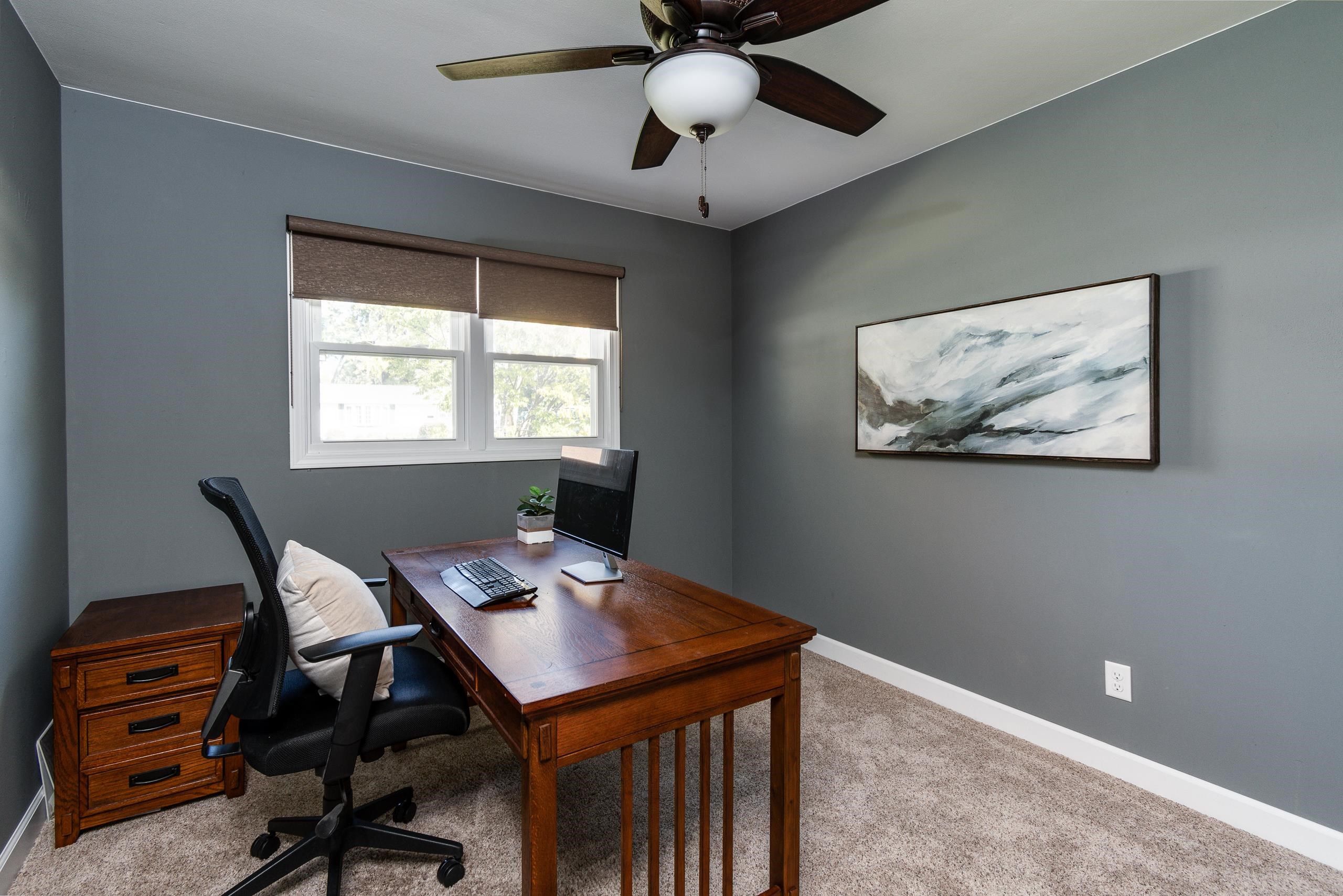 Furnished home office with a wooden desk, double window, and large abstract wall art.