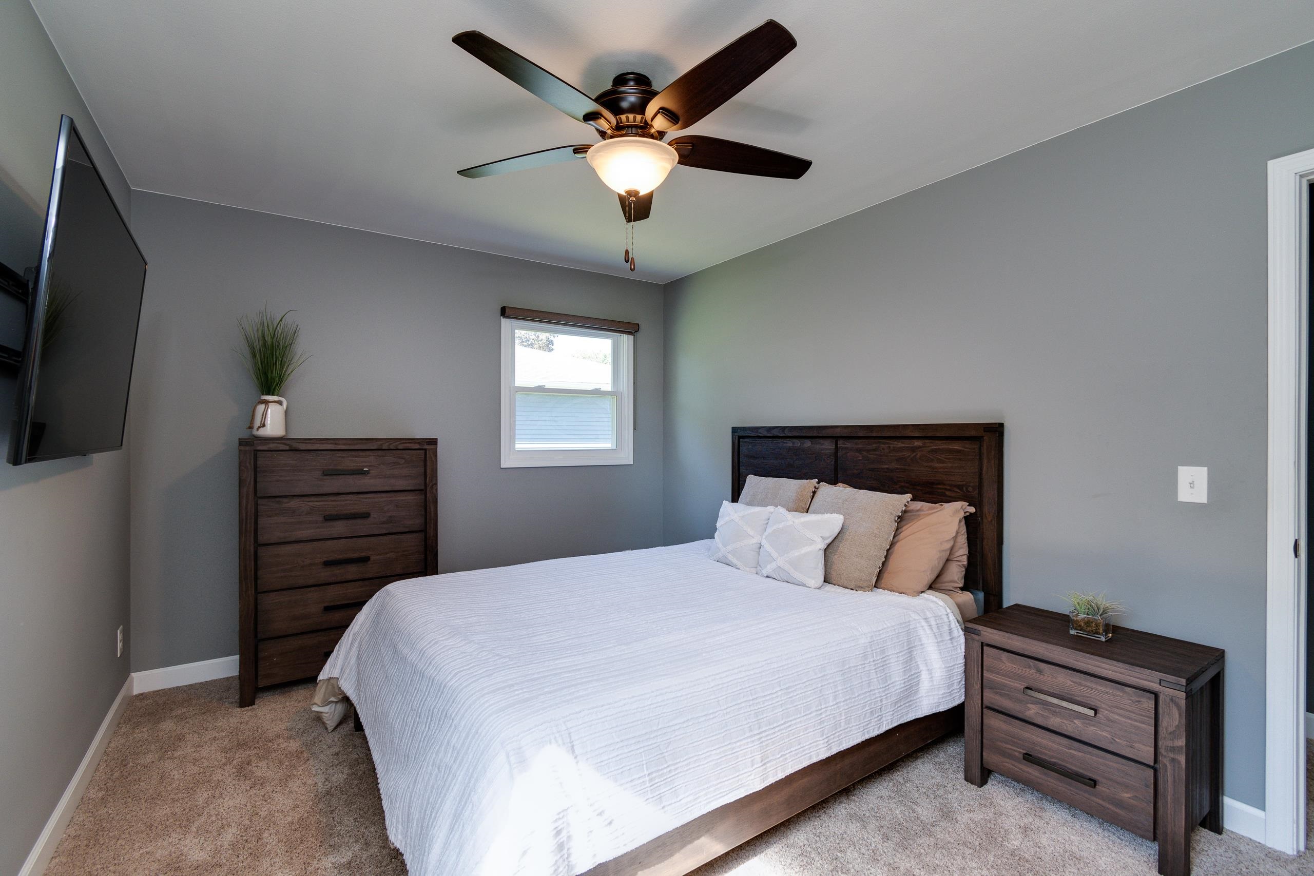 Staged bedroom with a dark wood bed, white bedding, matching furniture, and a ceiling fan.