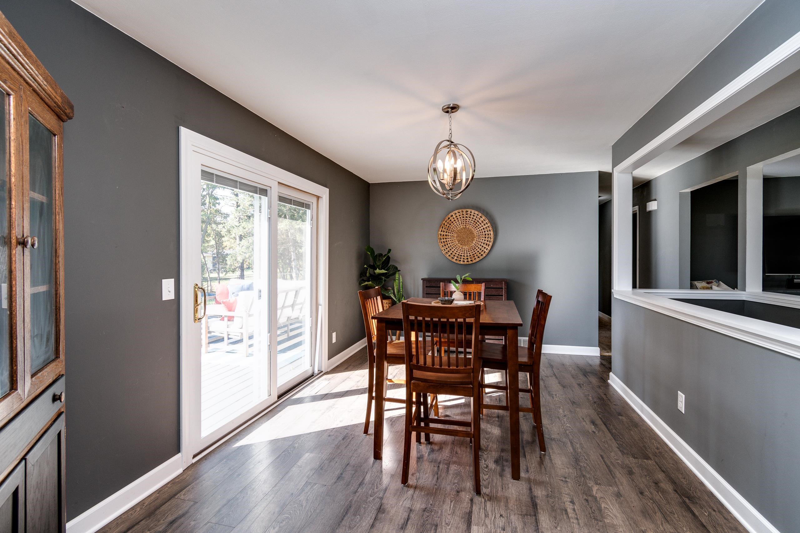 Dining room with a dark wood table, gray walls, and sliding glass doors opening onto a sunny deck.