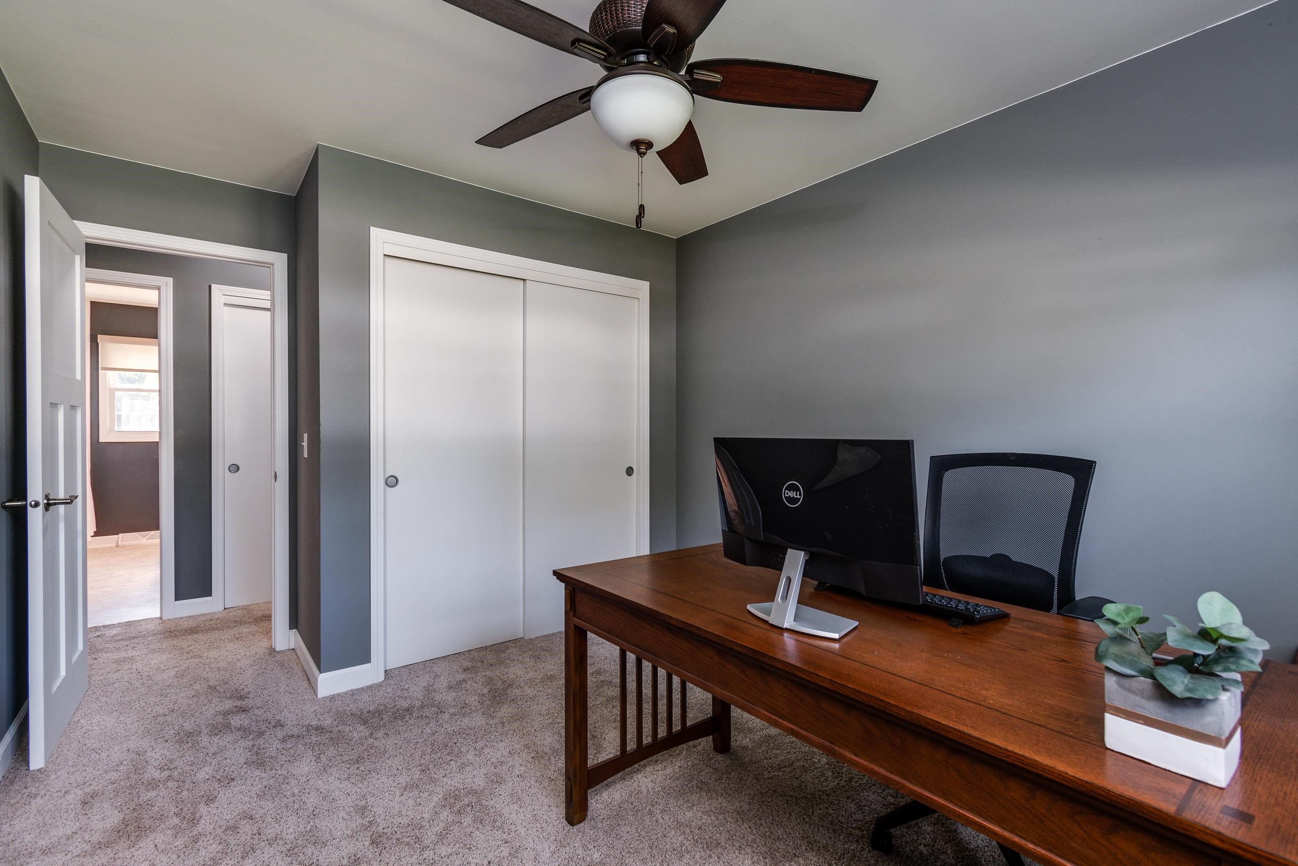 Home office with a dark wood desk and computer, gray walls, and white closet doors.