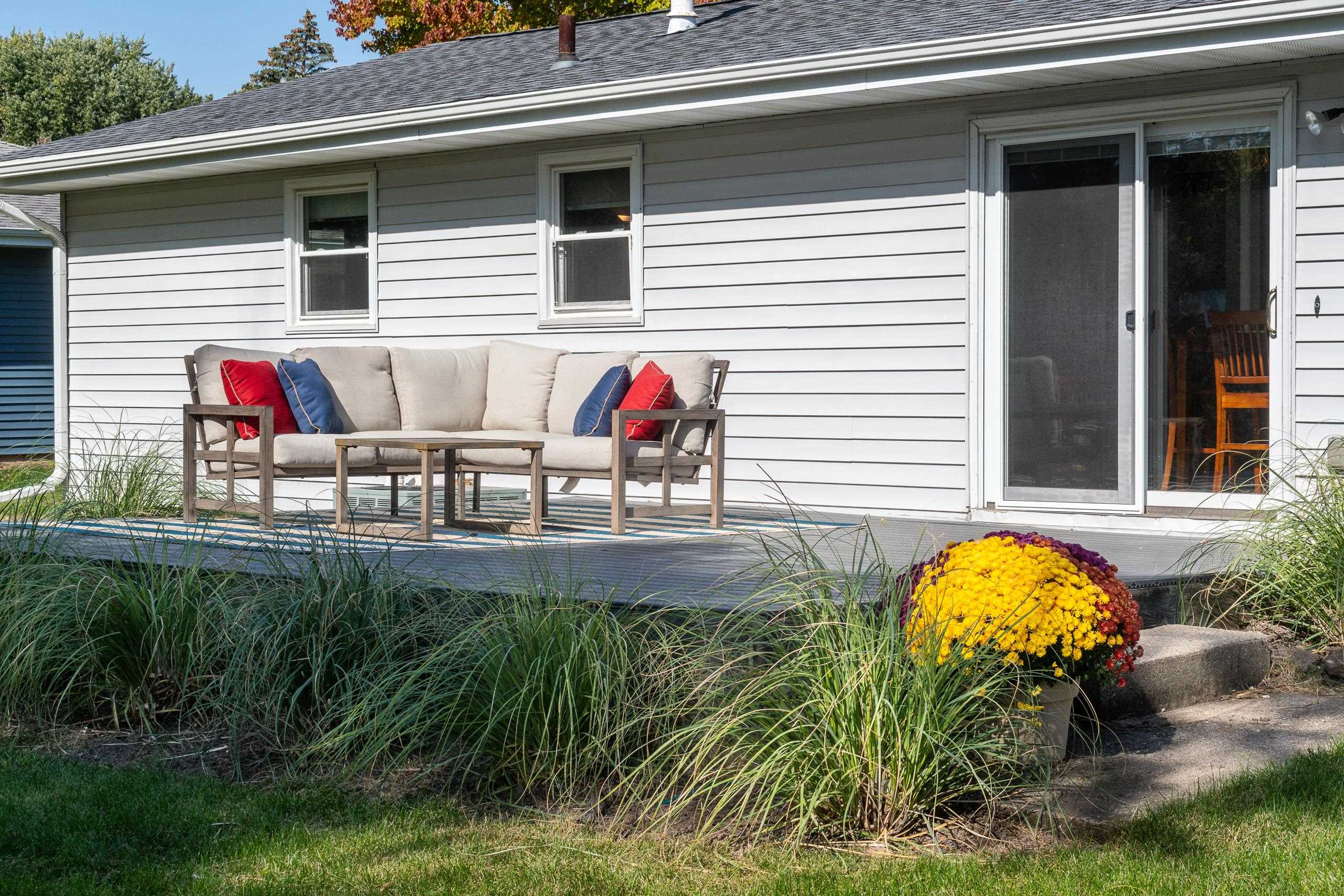 Raised patio with a cushioned sectional, sliding glass door, ornamental grasses, and a pot of yellow flowers.