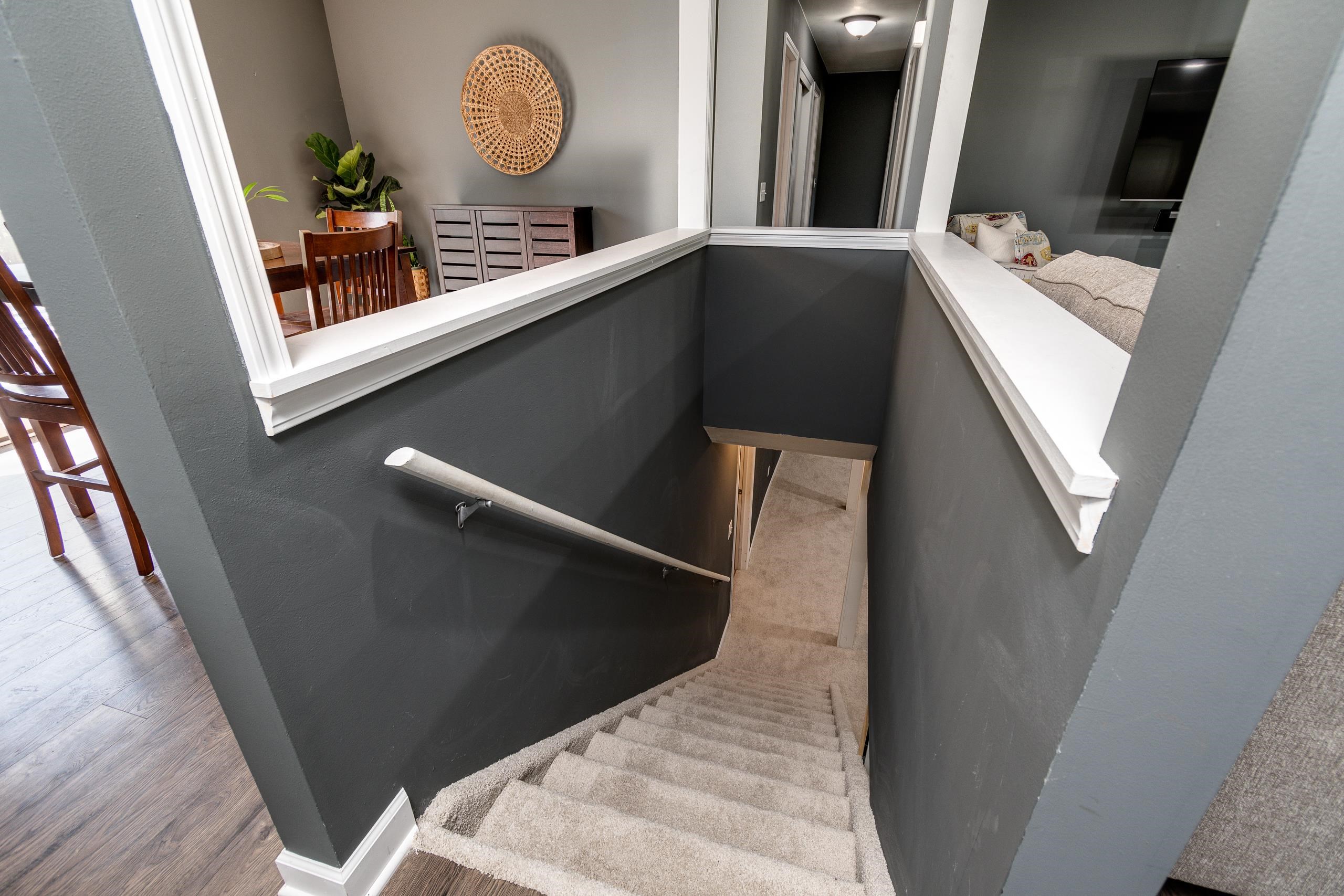 Carpeted staircase with dark gray walls, white handrail, and views of furnished rooms above.