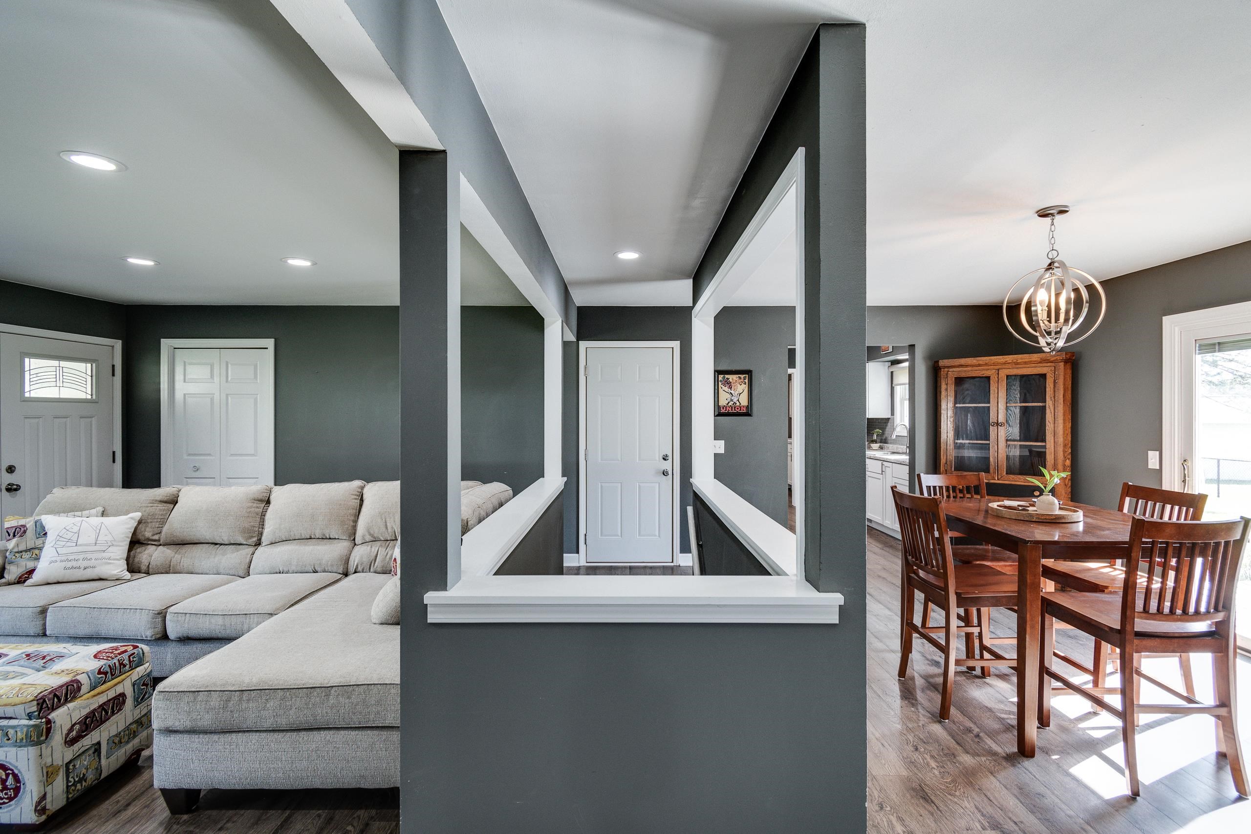 Living and dining area with a gray sectional, dark walls, and a wood dining set.