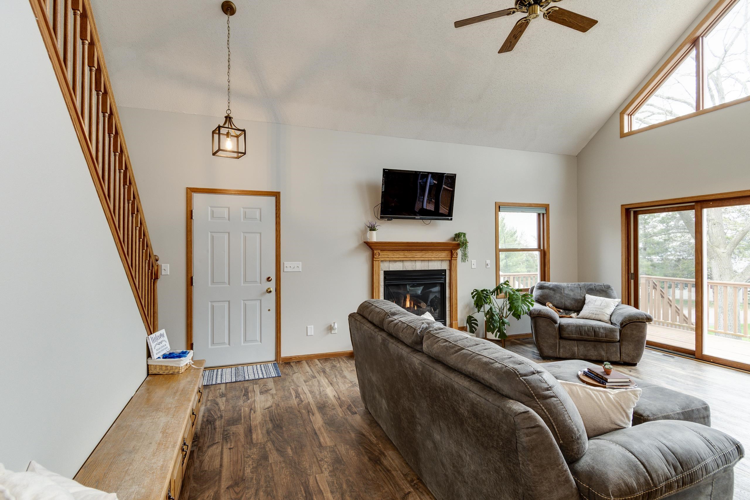 Living room with a vaulted ceiling, wood staircase, fireplace, and sliding doors to a deck.