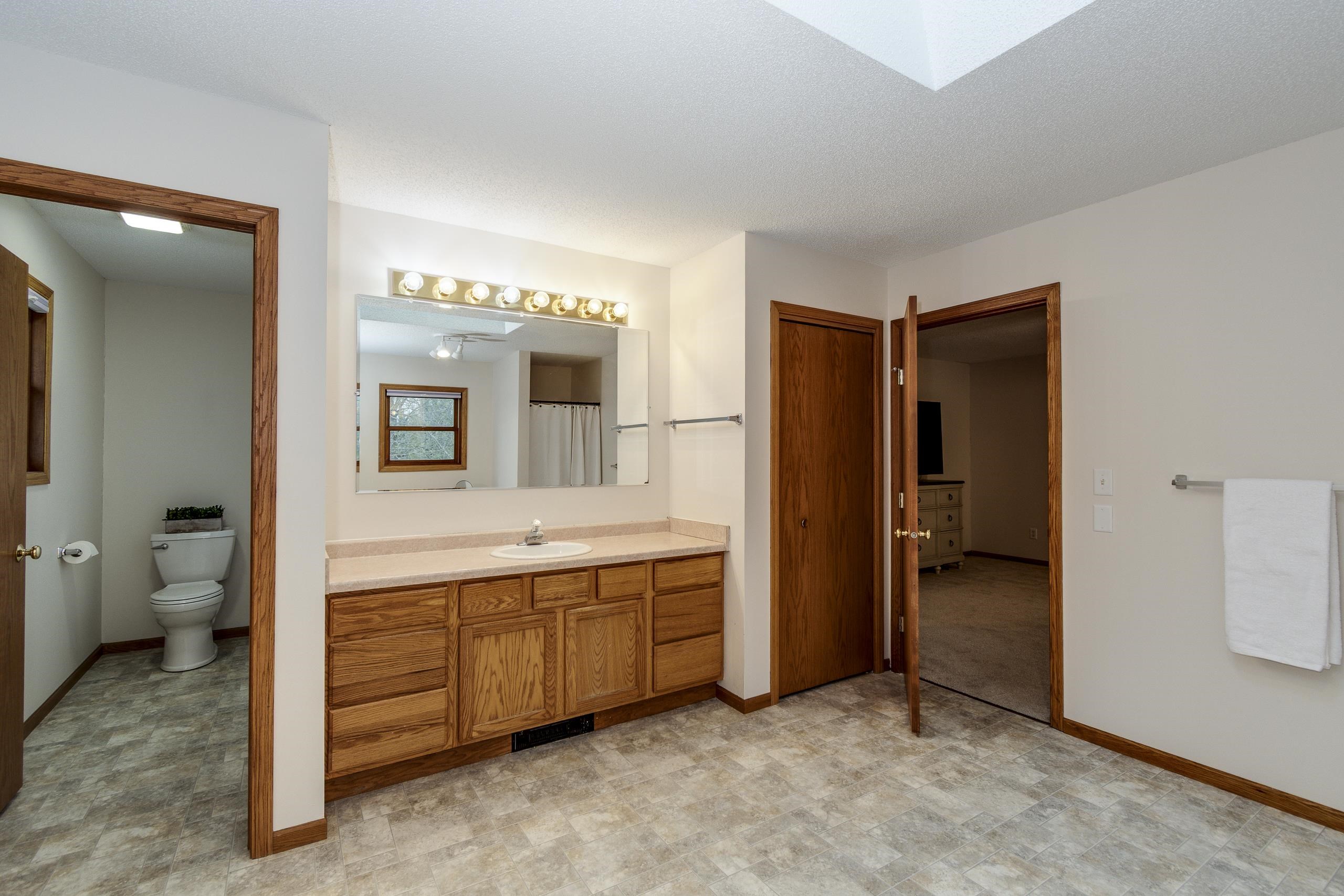 Bathroom with a long oak vanity and illuminated mirror beside a separate toilet alcove.