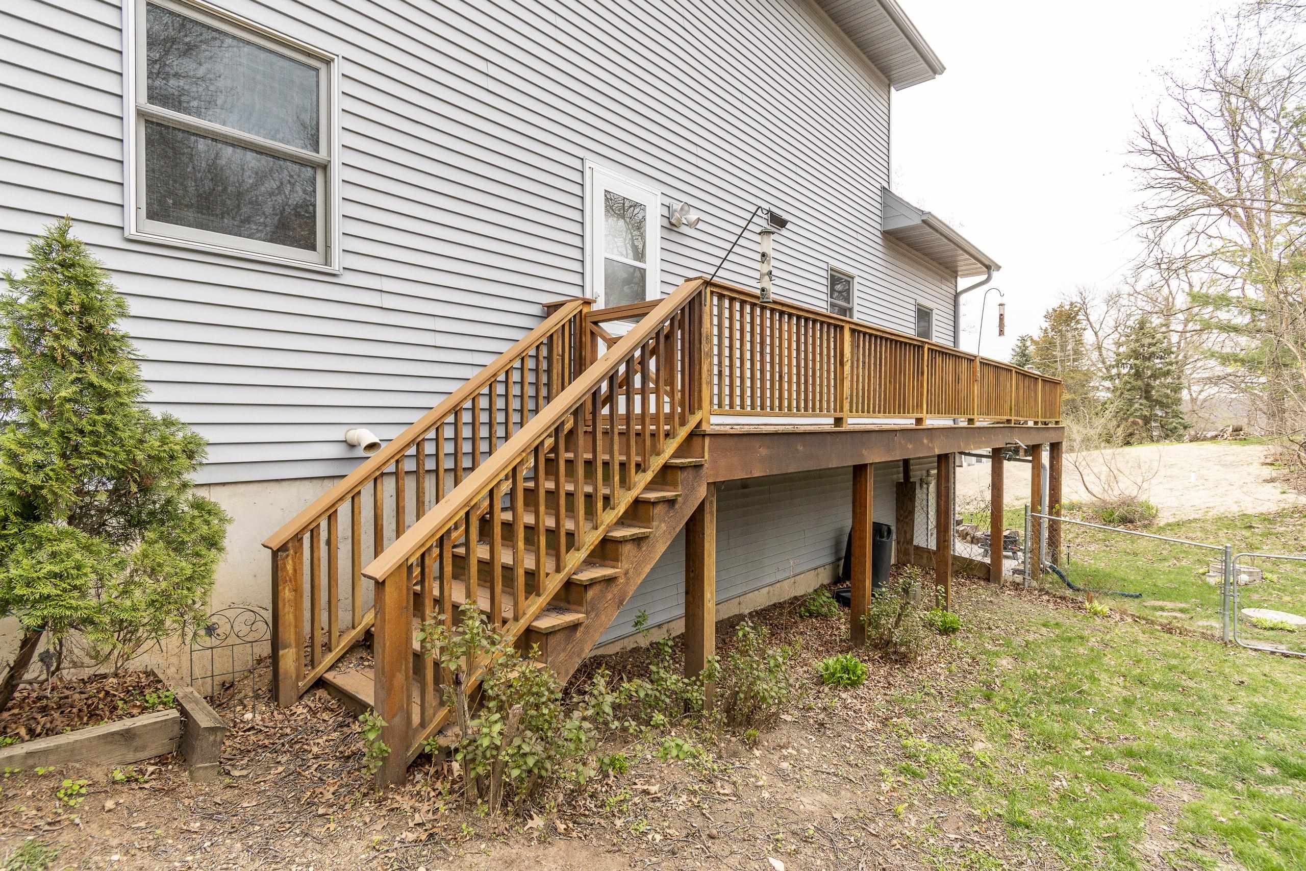 Raised wooden deck and staircase along the side of a gray-sided house.