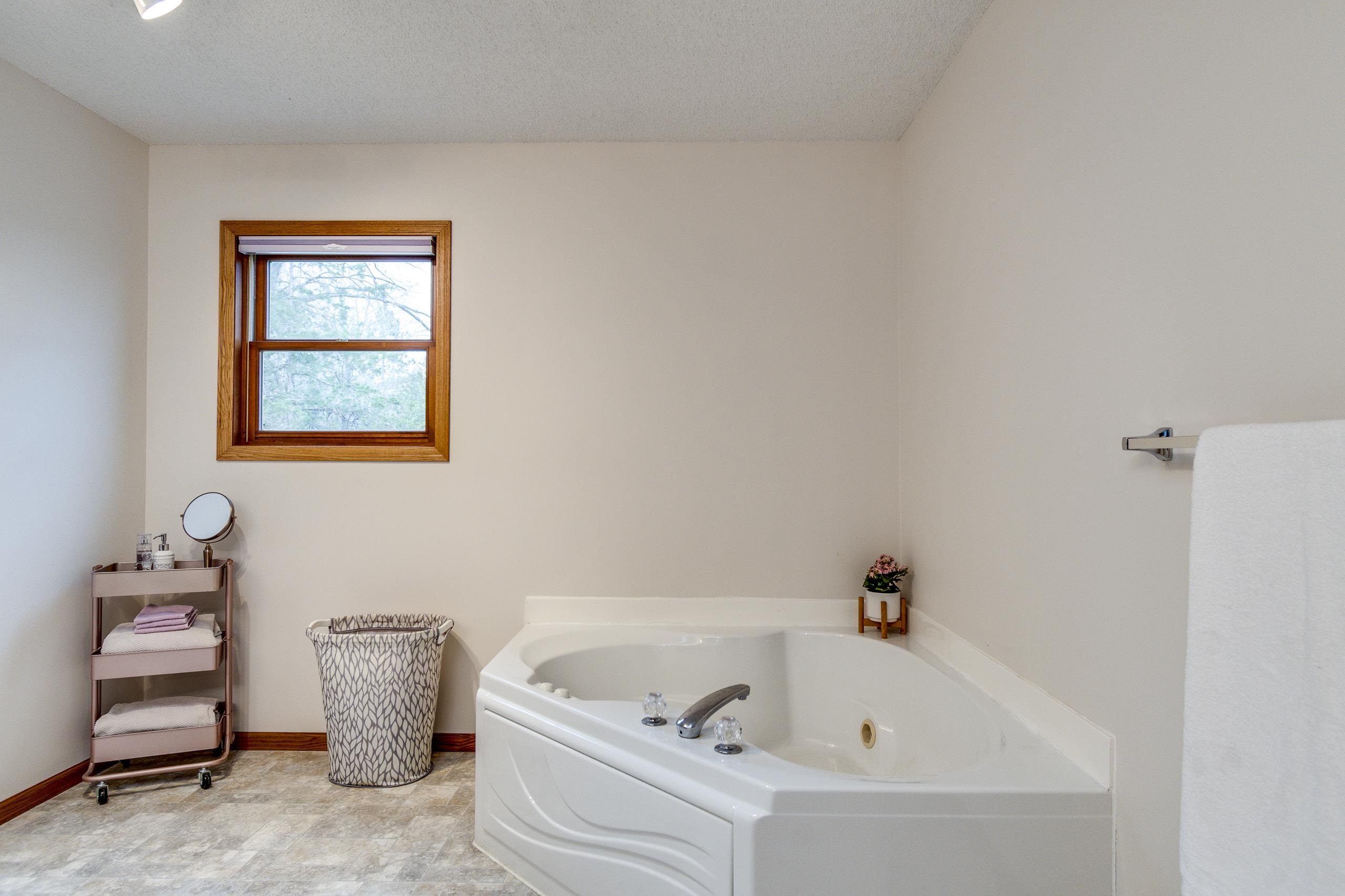 Bathroom with a large corner jetted tub beneath a wood-trimmed window.