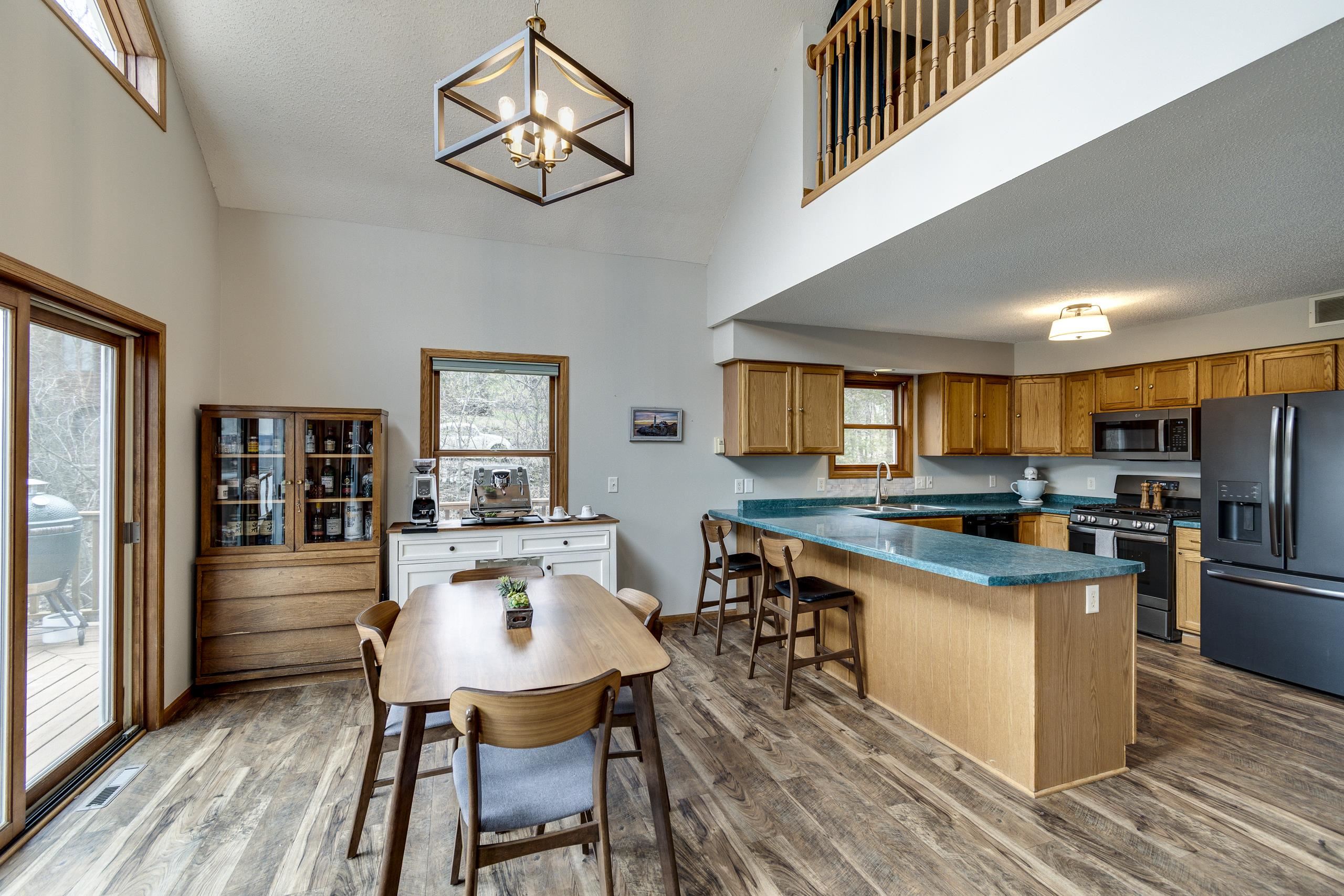 Open-plan kitchen and dining area with a turquoise island, wood cabinets, and vaulted ceiling.