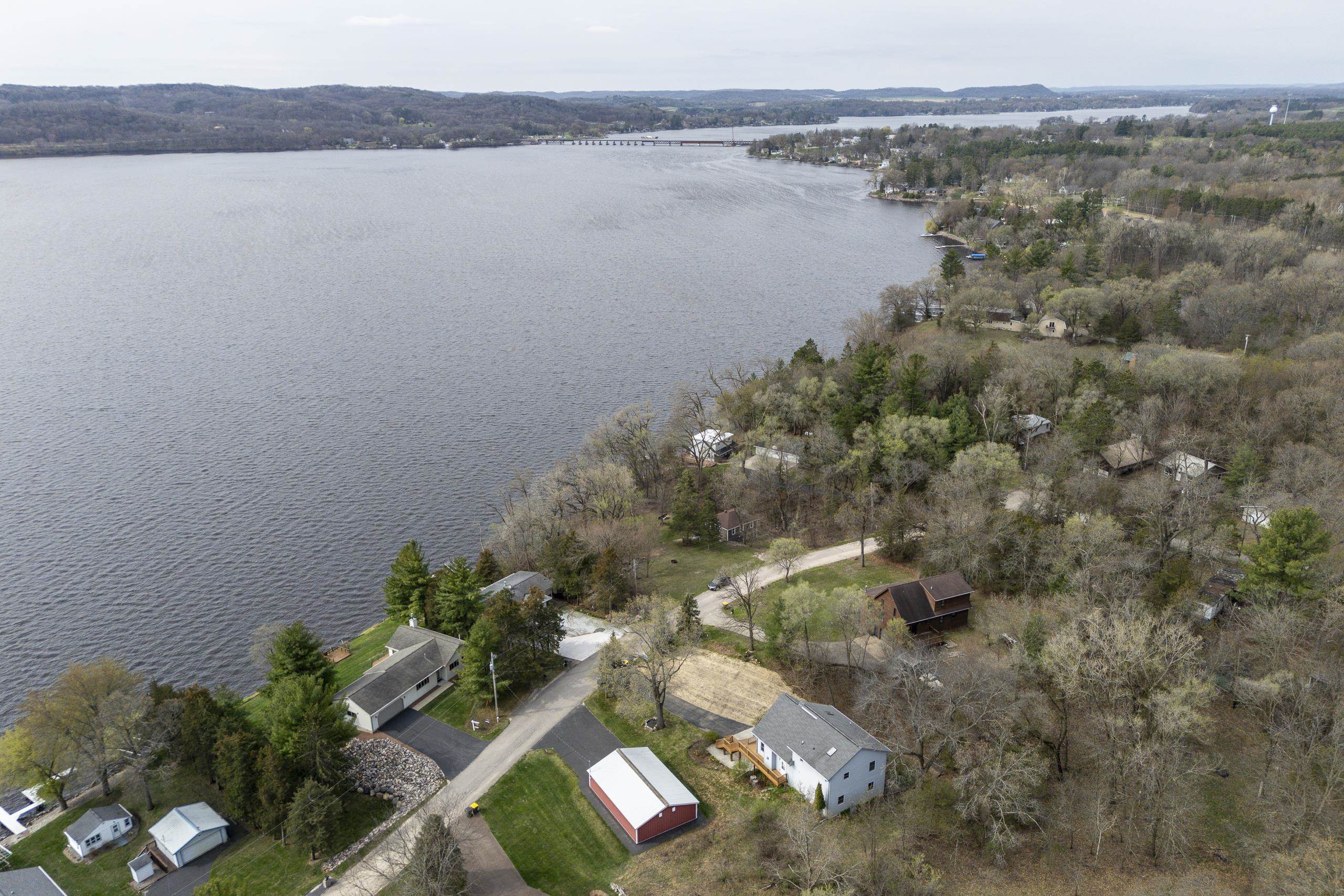 Aerial view of lakeside homes and wooded shoreline beside a broad lake, with a bridge in the distance.