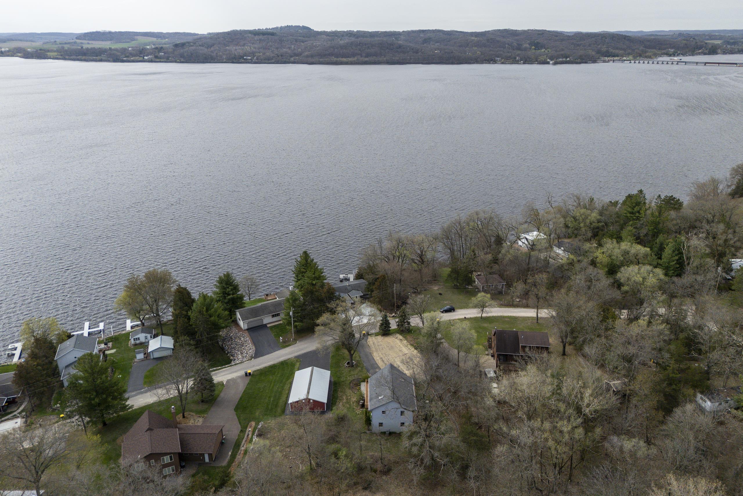 Aerial view of lakeside homes and docks along a wooded shoreline, with rolling hills across the water.