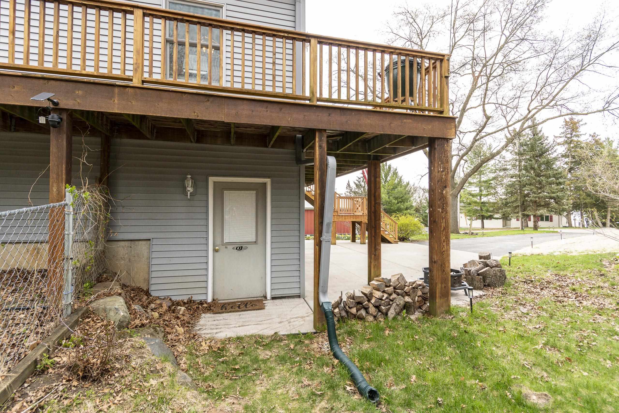 Gray home with a raised wood deck, ground-level entry, and firewood stacked beside the patio.